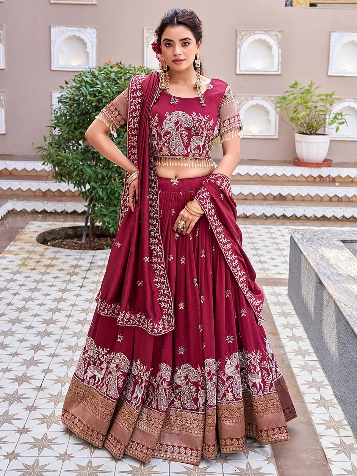 Woman wearing a maroon designer lehenga choli with intricate gold embroidery and a matching dupatta