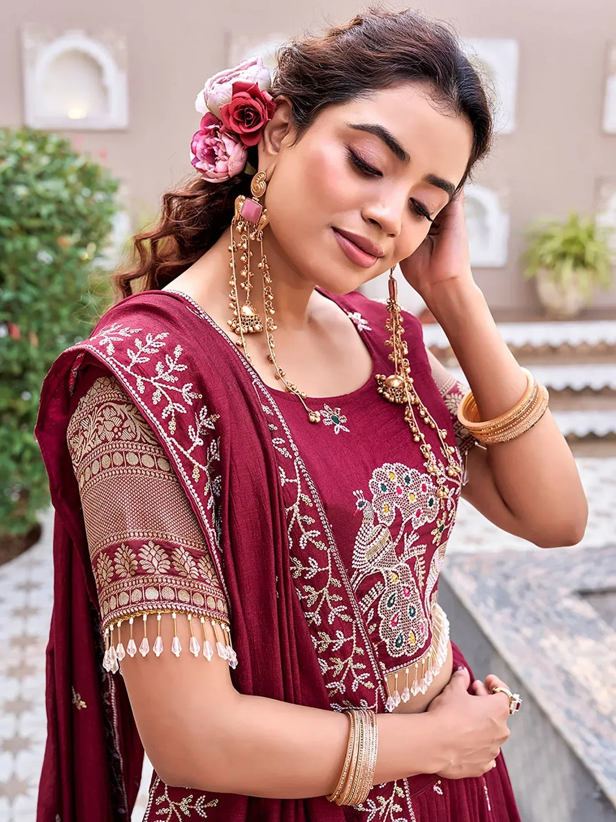 Woman wearing a maroon embroidered ethnic salwar kameez with gold jewelry and floral hair accessory