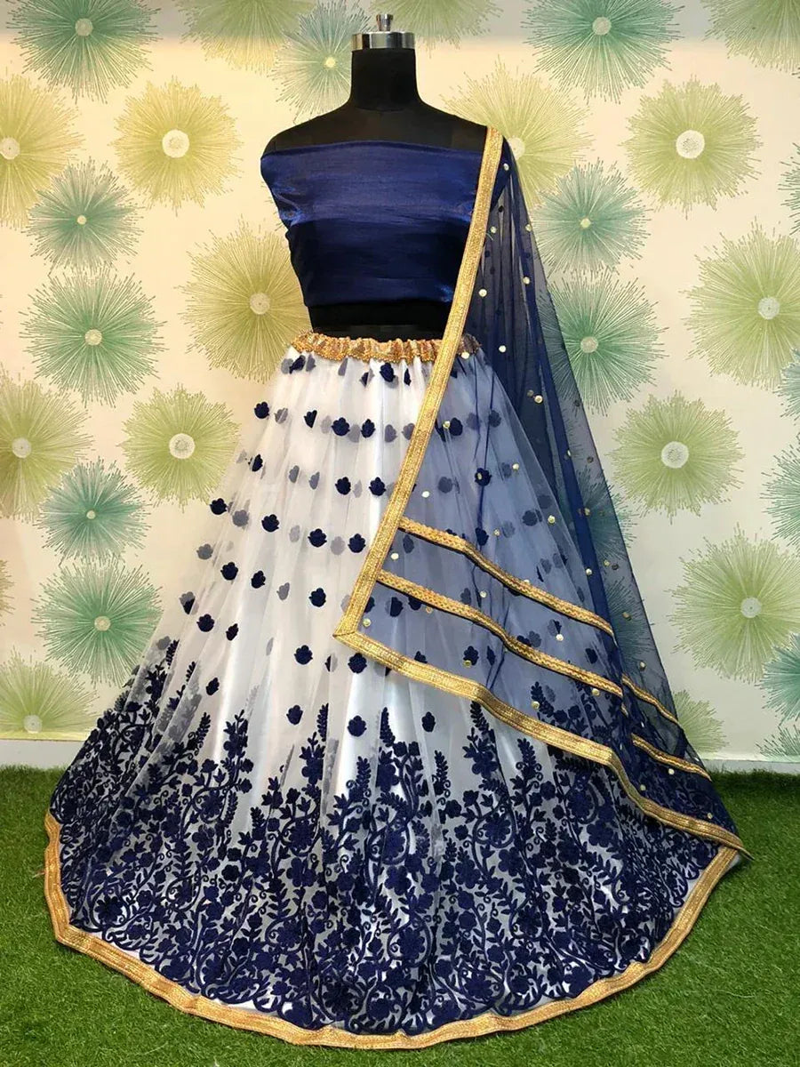Blue and white embroidered lehenga choli with gold trim, displayed on mannequin against floral backdrop