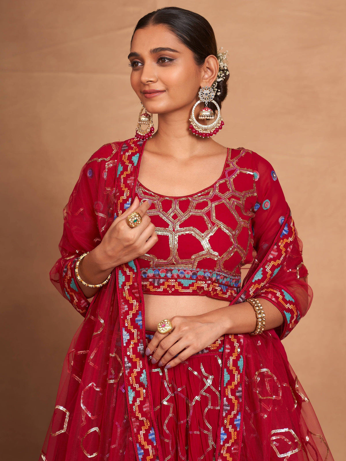 Red embroidered lehenga choli with gold and blue detailing, paired with statement earrings