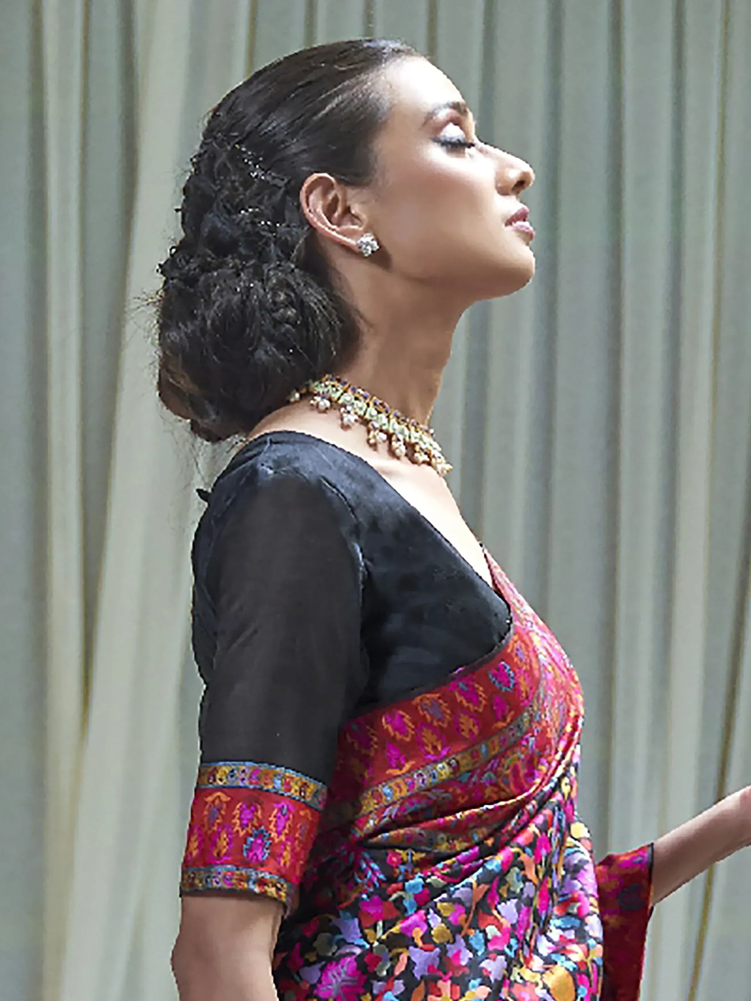 Woman in vibrant floral saree with black blouse, elegant updo, and traditional jewelry