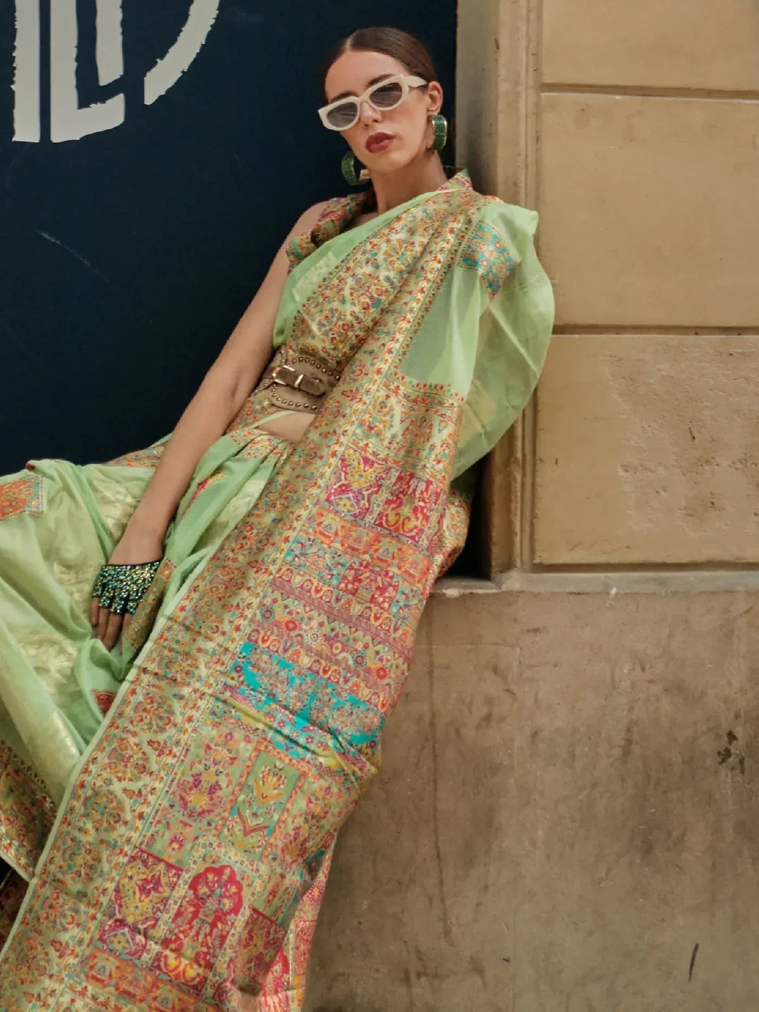 Stylish woman in mint green printed saree with bold belt, modern sunglasses, and statement earrings