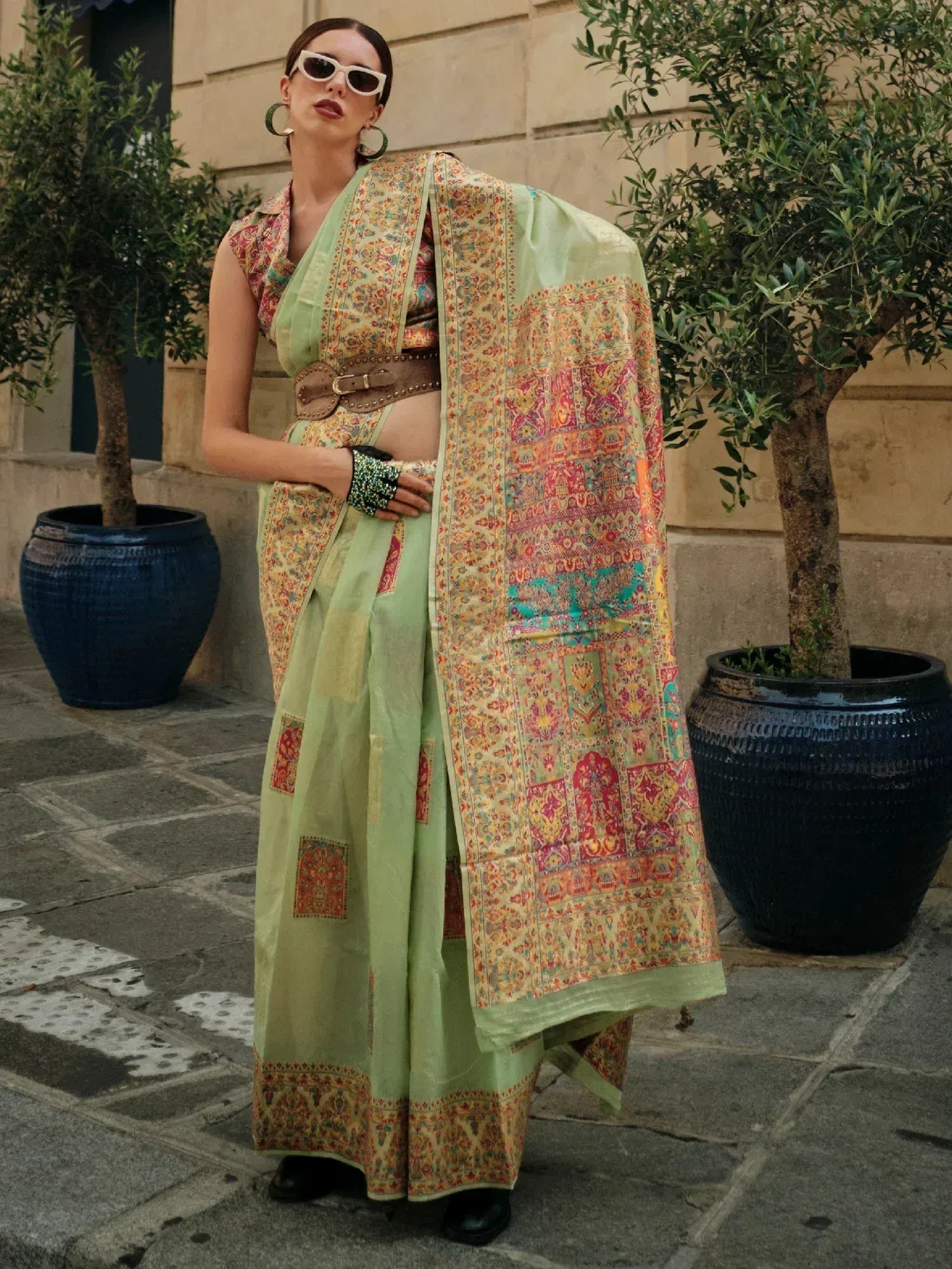 Stylish green printed saree with ethnic motifs, modern belt, and statement accessories for contemporary Indian wear