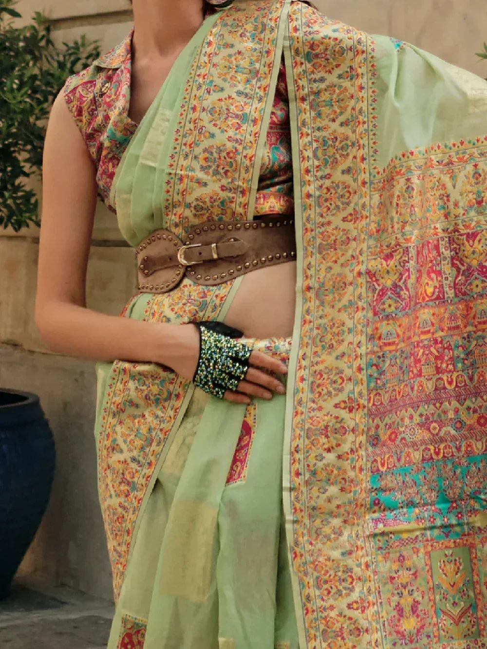 Mint green printed saree with floral border, studded belt, and embellished hand accessory