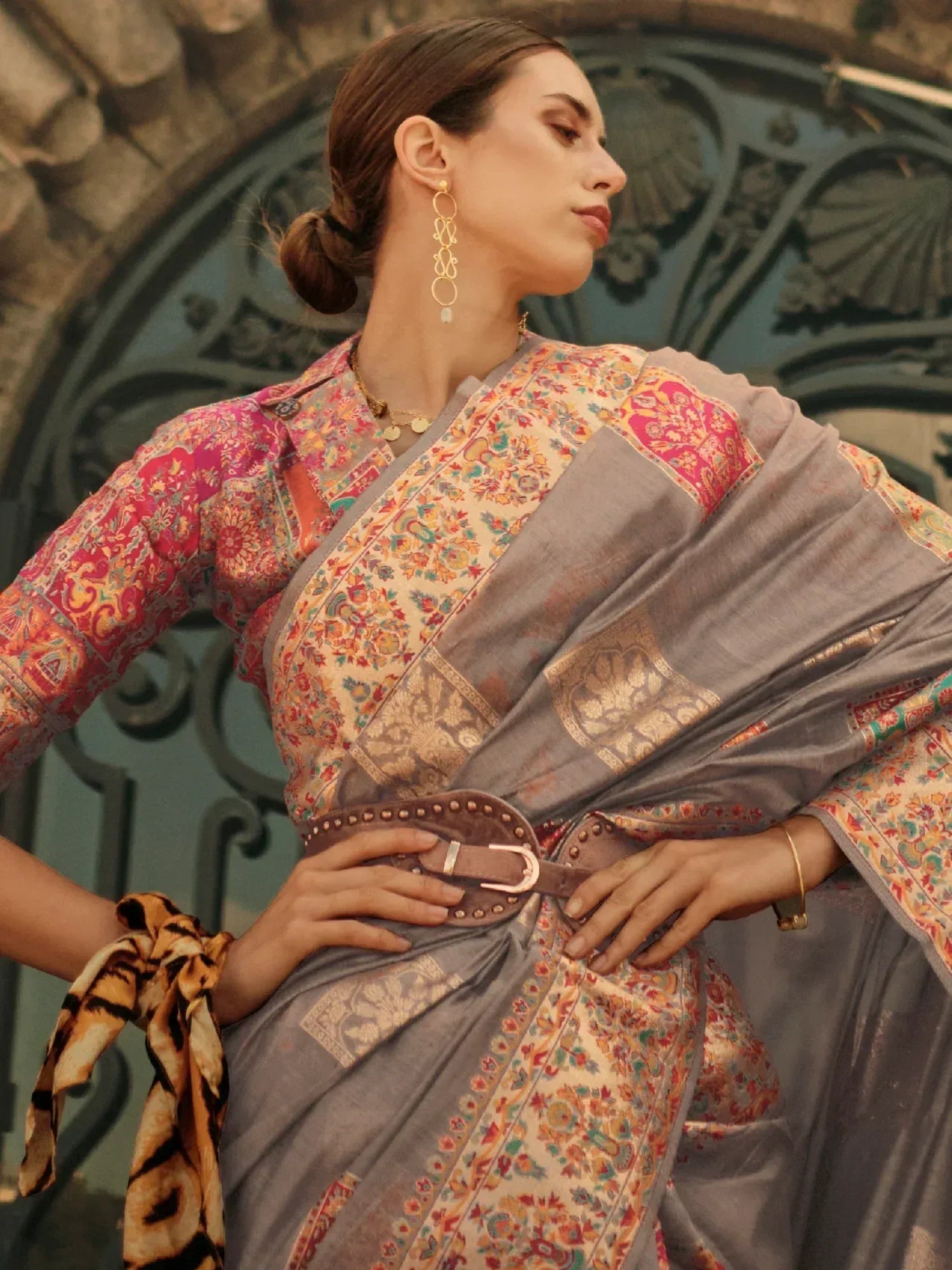 Woman in floral printed saree with grey border and belt, styled with gold earrings and tiger print scarf