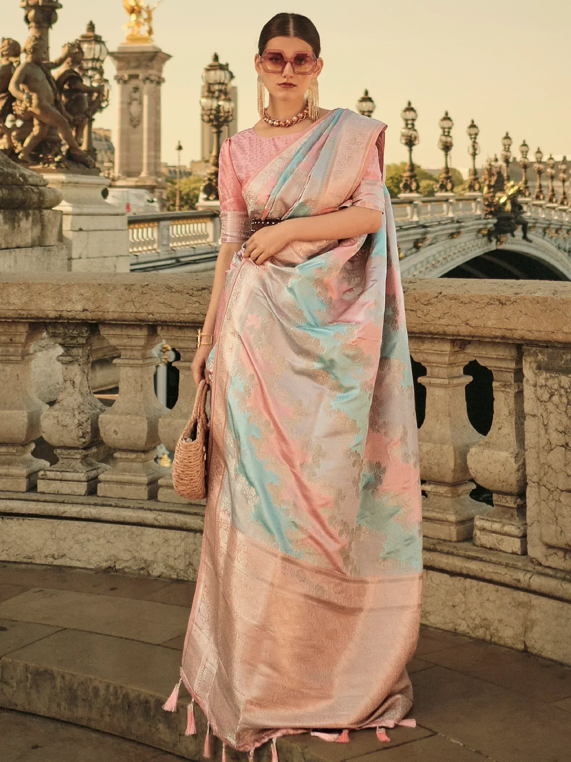 Woman in pastel pink and blue designer saree with gold motifs, styled for ethnic wear on a bridge