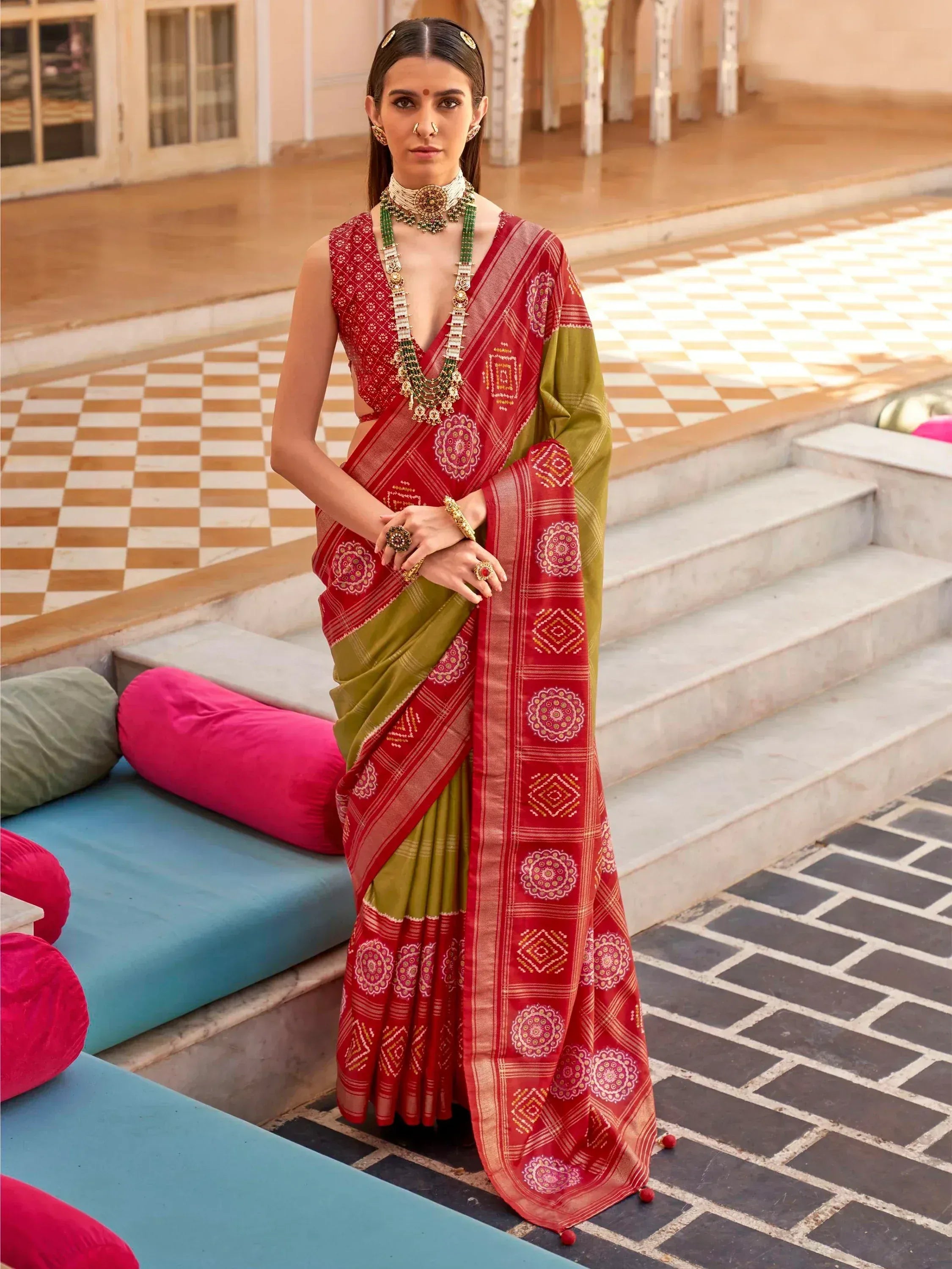 Red and olive green ethnic saree with intricate geometric and floral prints, paired with traditional jewelry for festive occasions.