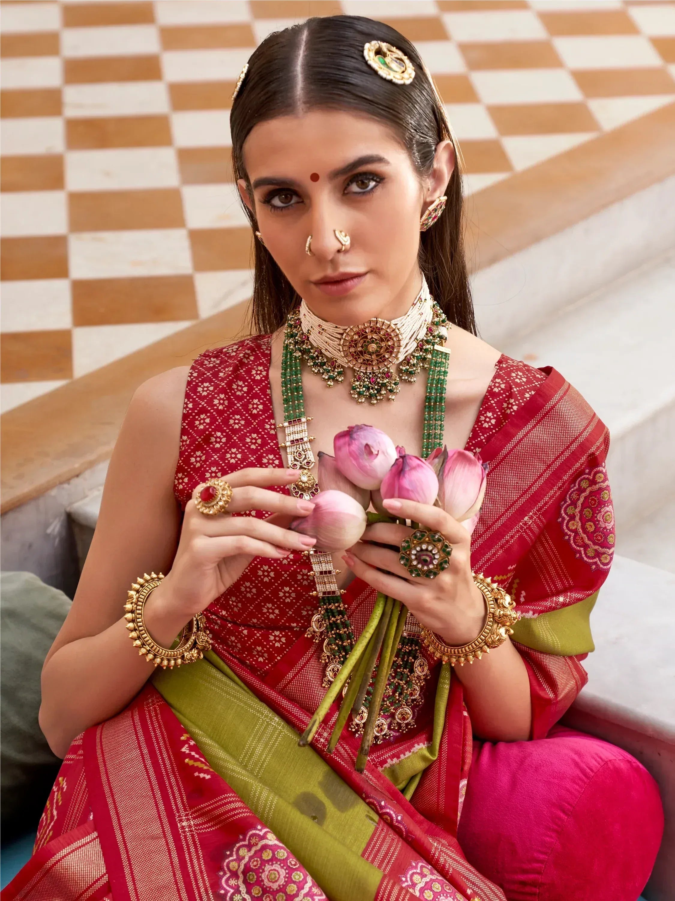 Woman in red and green ethnic saree with traditional jewelry holding lotus flowers