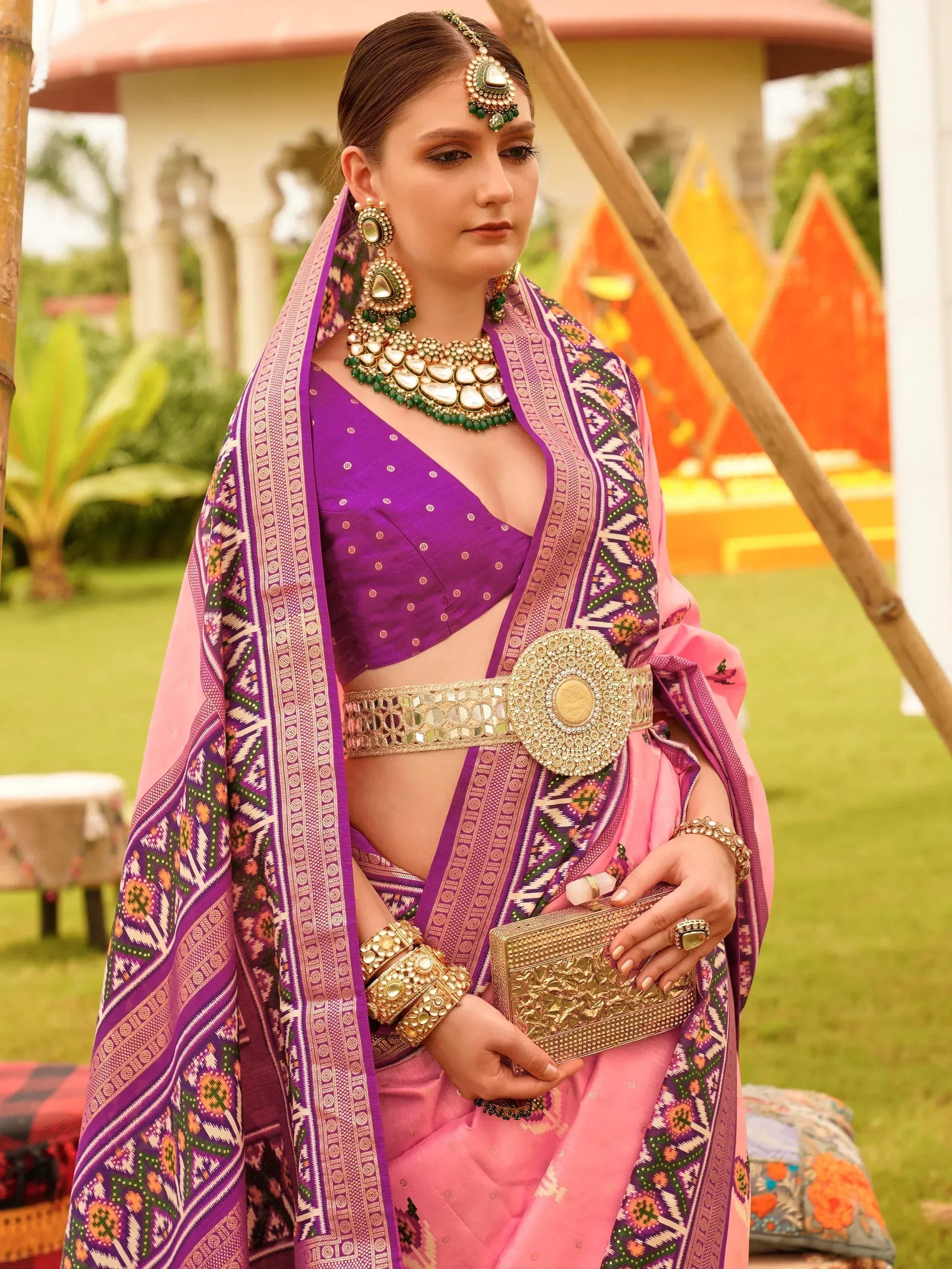 Woman in purple and pink ethnic saree with gold jewelry and mirror work belt, perfect for Indian festivals.