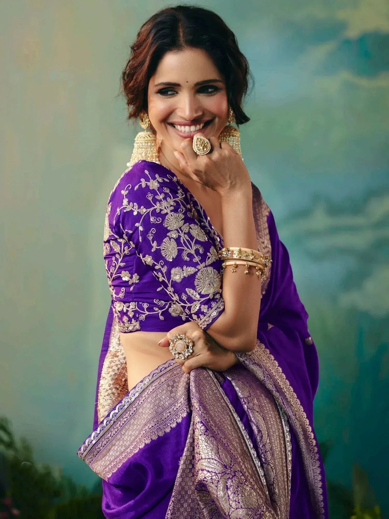 Woman in purple embroidered saree with gold jewelry, showcasing ethnic Indian fashion.