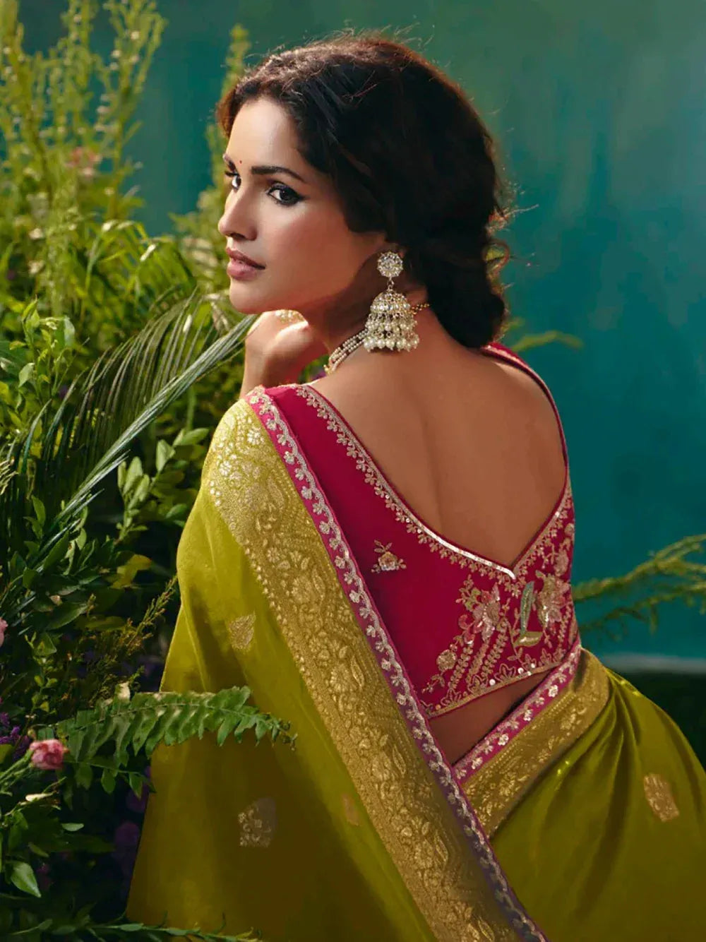 Woman in vibrant green saree with red embroidered blouse, traditional Indian ethnic wear, floral backdrop