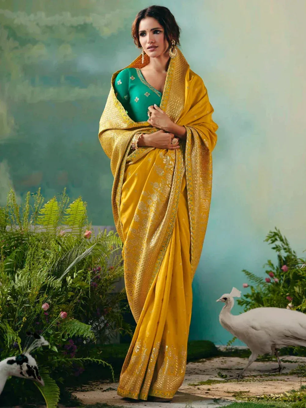 Woman in elegant yellow designer saree with green blouse, floral embroidery, and peacock backdrop