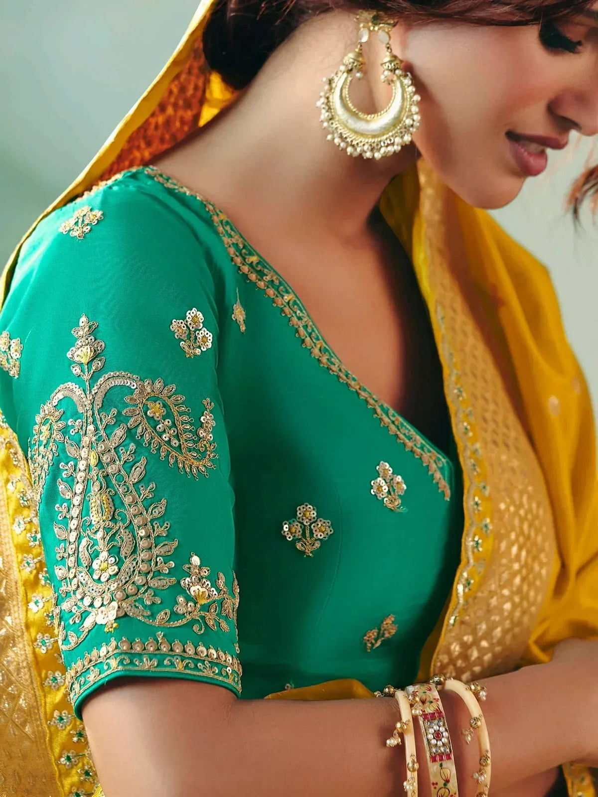 Emerald green embroidered choli with gold detailing, paired with yellow dupatta and traditional earrings