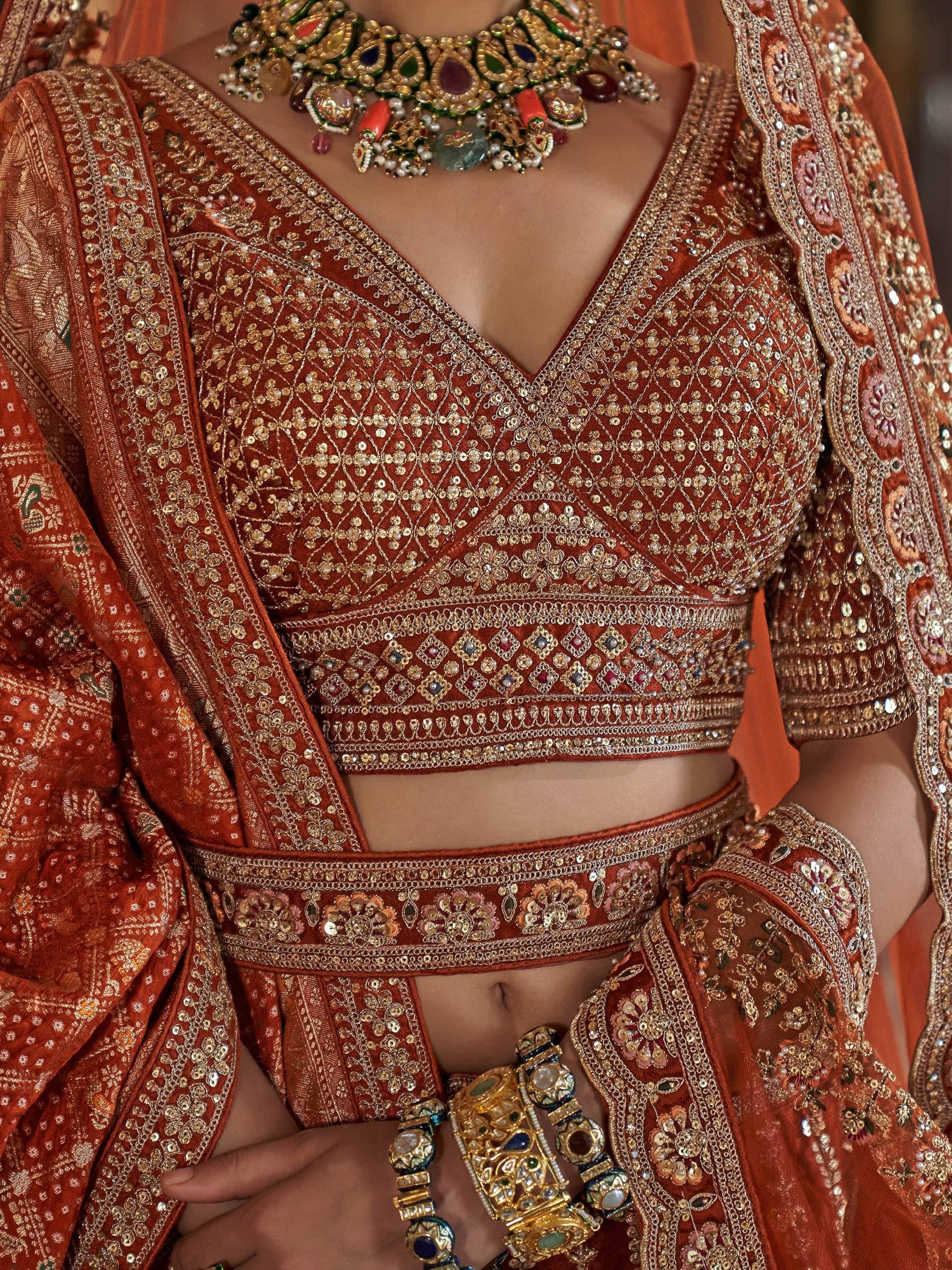 Rust orange designer lehenga choli with heavy gold embroidery and traditional jewelry