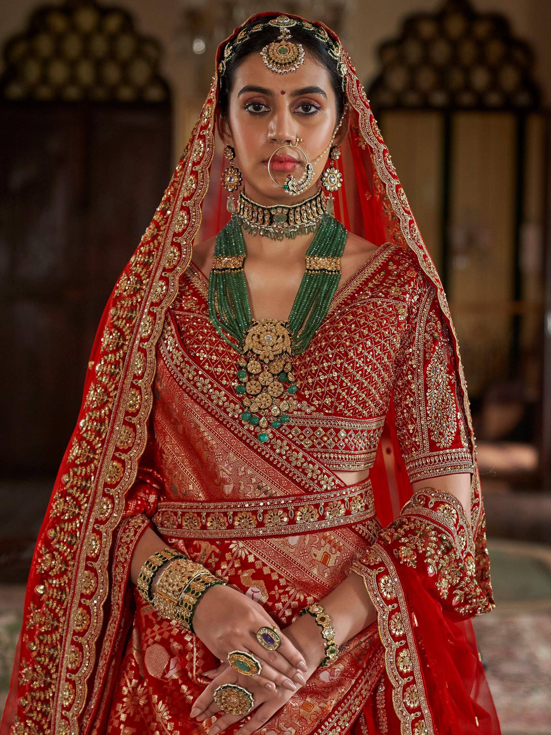 Red embroidered lehenga choli with green jewelry and traditional Indian bridal accessories