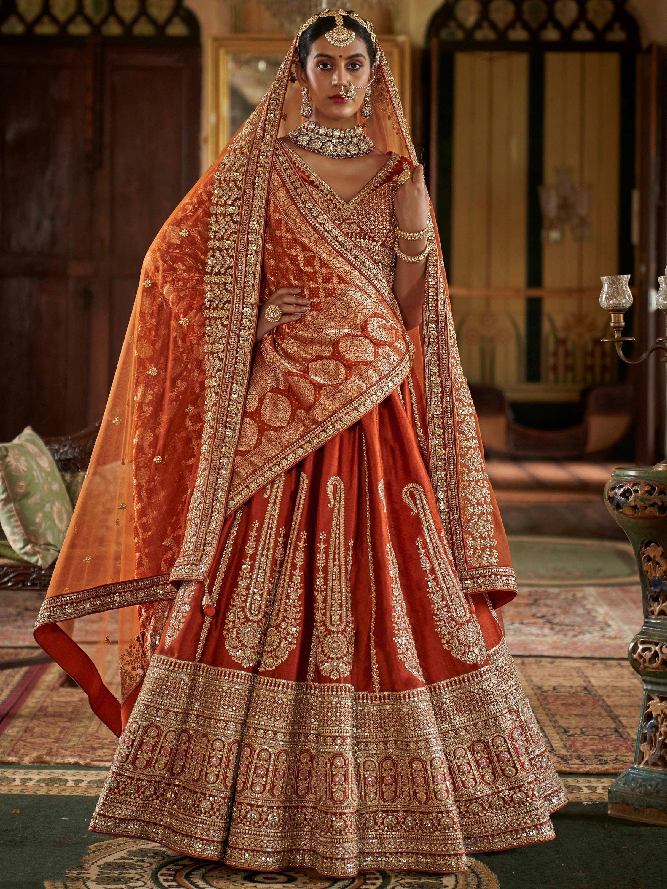 Luxury Indian bridal lehenga choli in rust with heavy gold embroidery and dupatta, perfect for weddings.