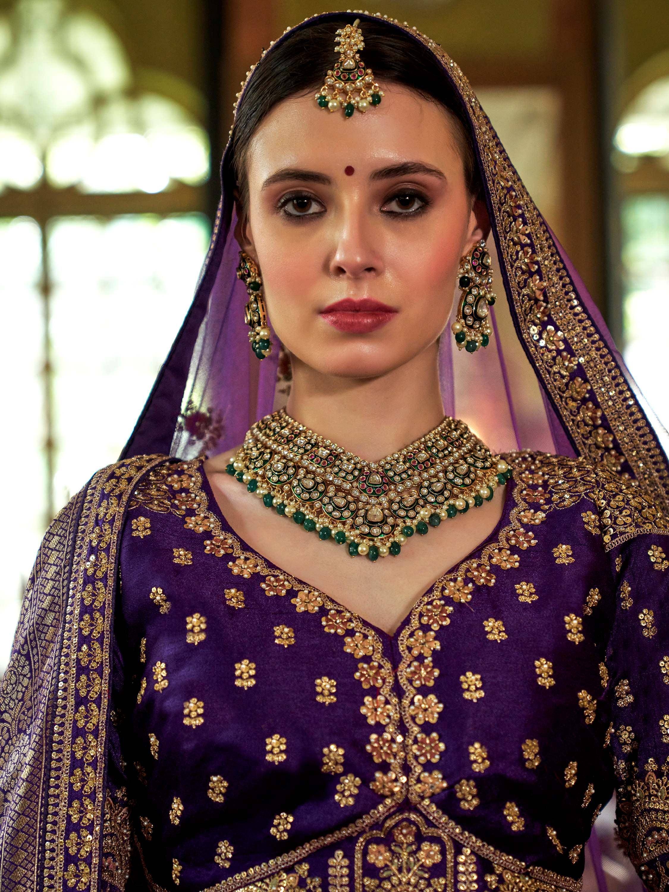 Purple Indian bridal lehenga with gold embroidery and emerald jewelry set
