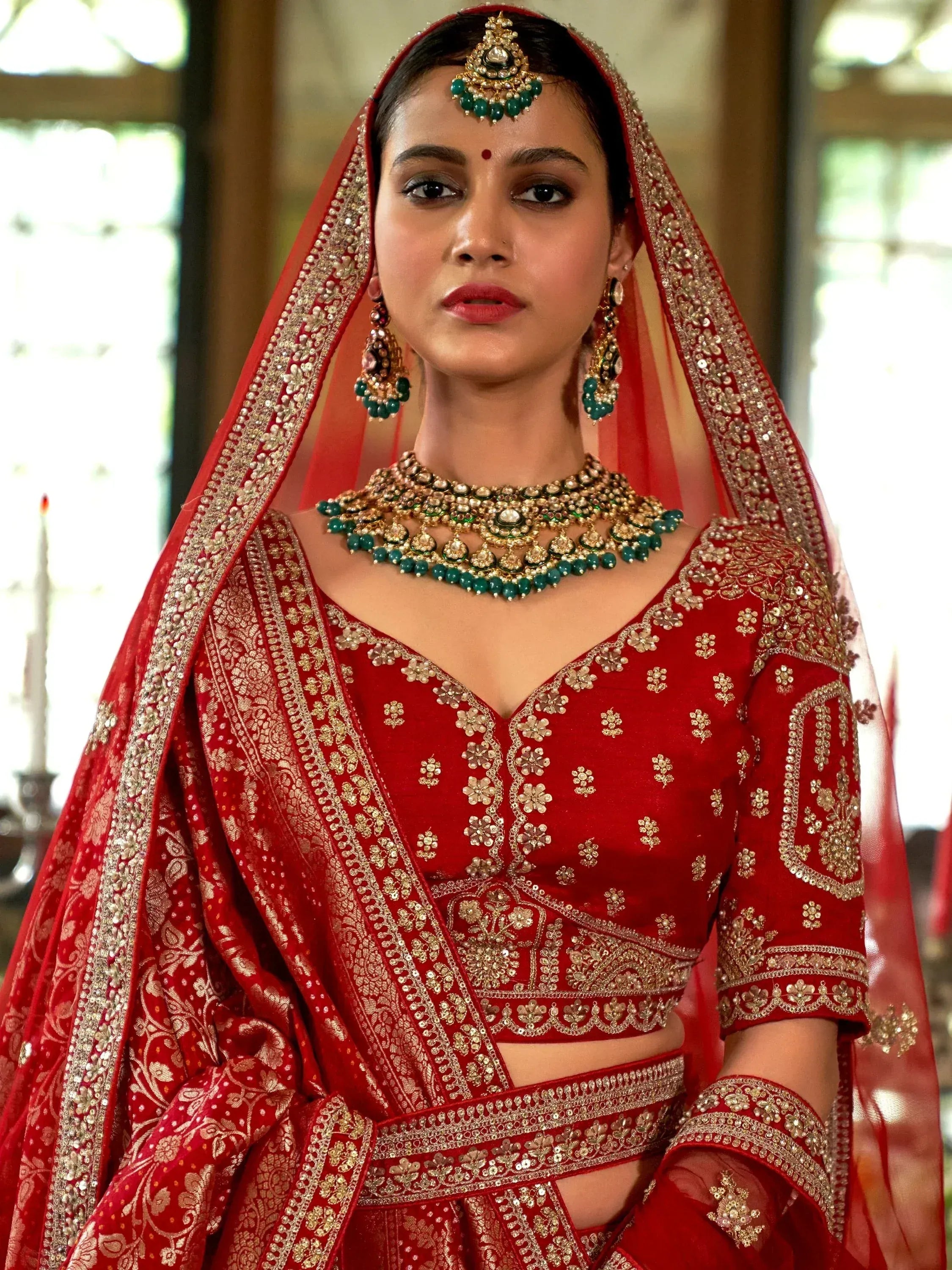 Red embroidered lehenga choli with gold detailing, green jewelry, and matching dupatta for Indian weddings
