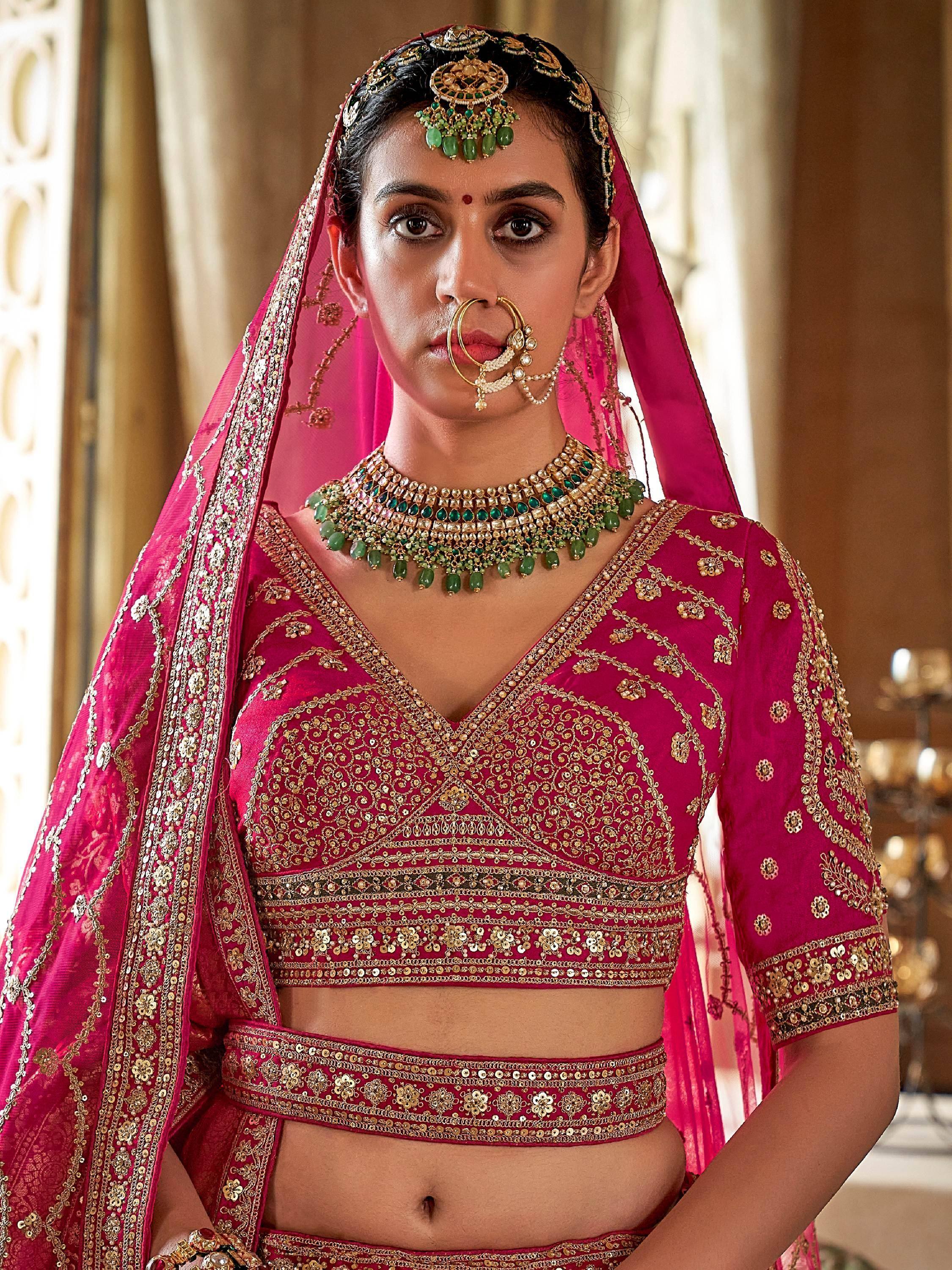 Pink embroidered lehenga choli with gold detailing and green jewelry for Indian weddings