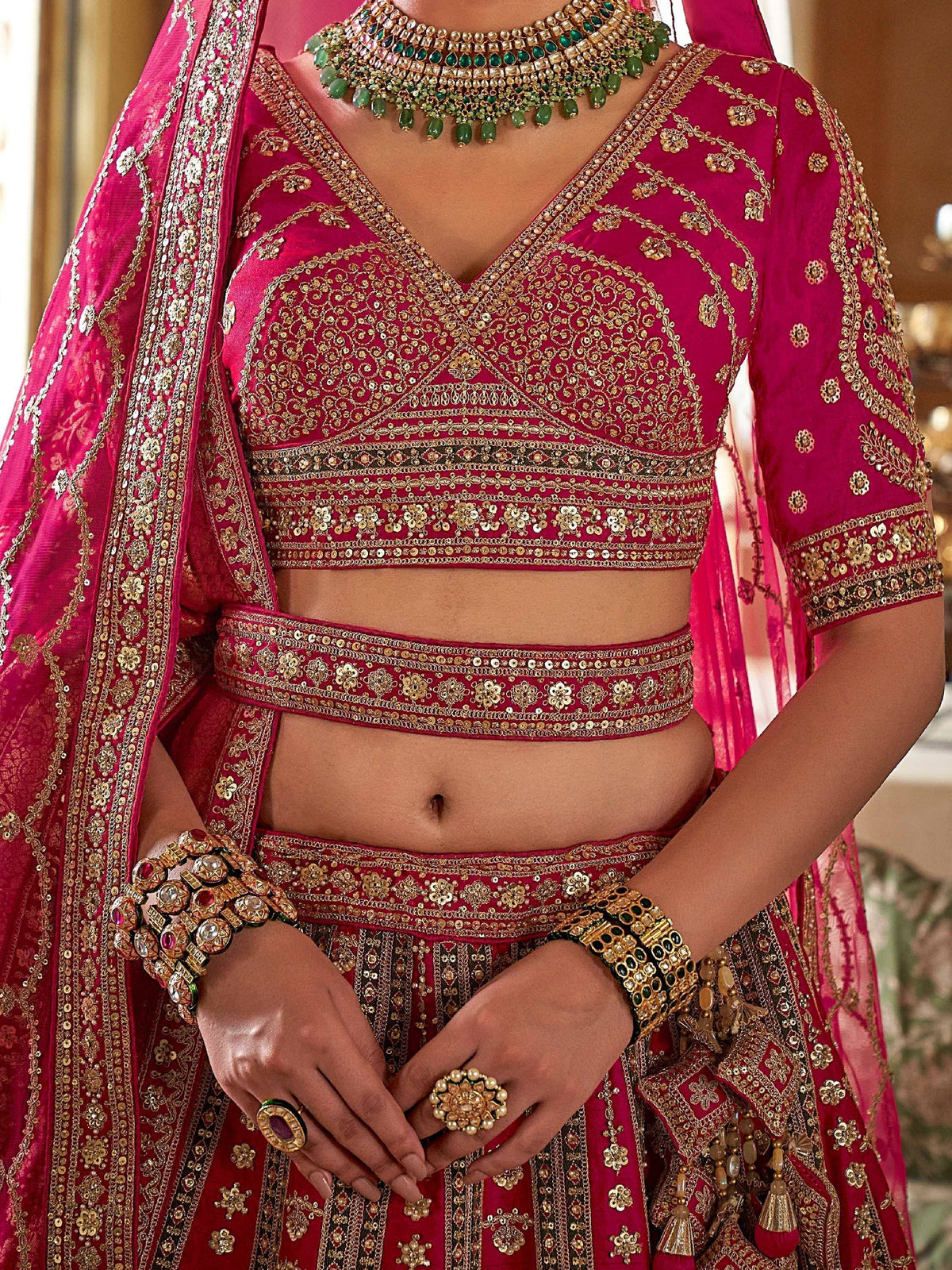 Fuchsia Indian bridal lehenga choli with gold embroidery, sequins, and green stone jewelry