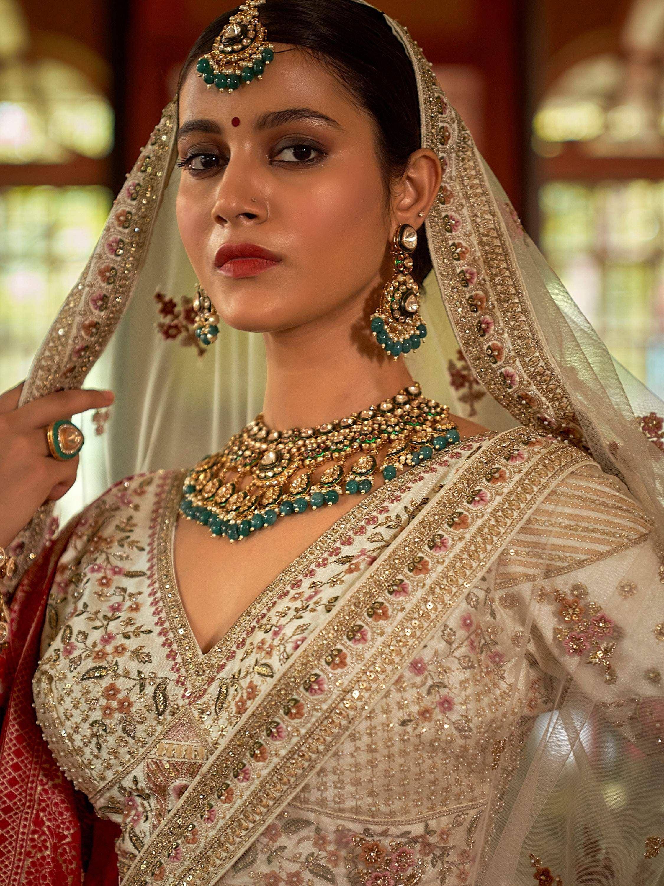 Elegant Indian bride in embroidered lehenga choli with gold and green jewelry, perfect for weddings.