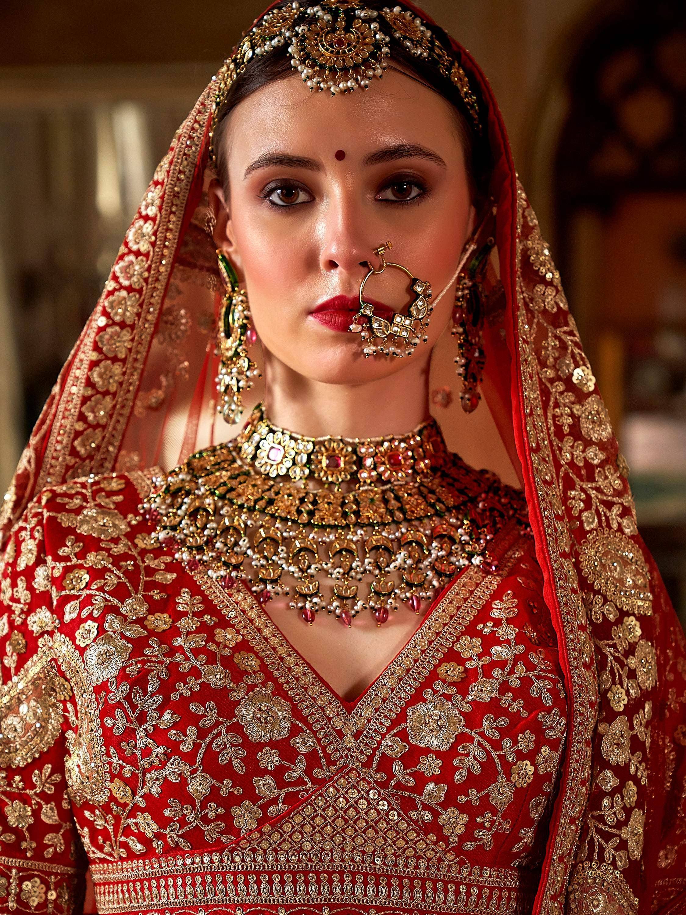 Red bridal lehenga choli with gold embroidery, maang tikka, and traditional Indian jewelry for wedding