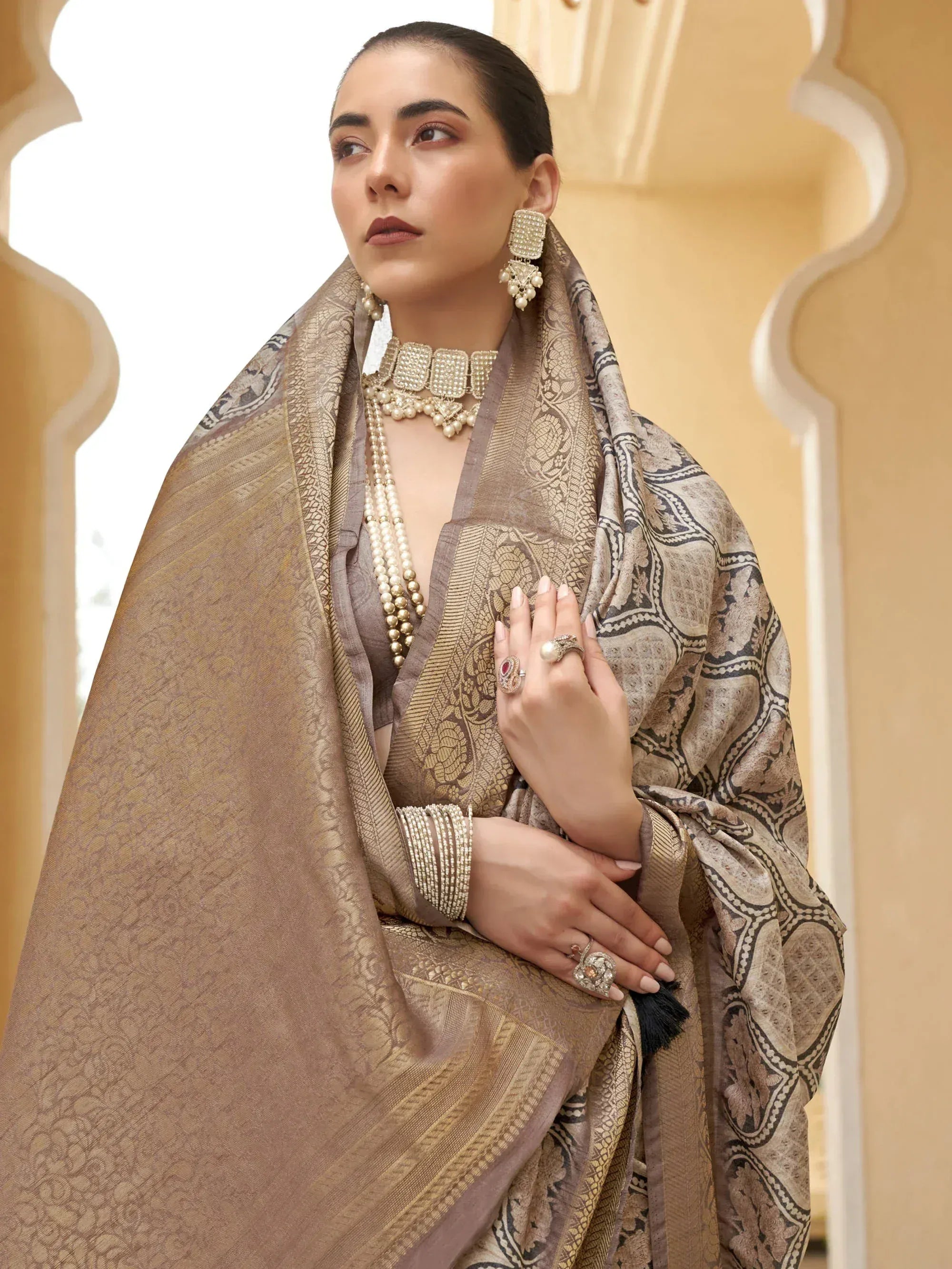 Elegant woman in designer Indian saree with intricate gold patterns, paired with pearl jewelry and traditional earrings.