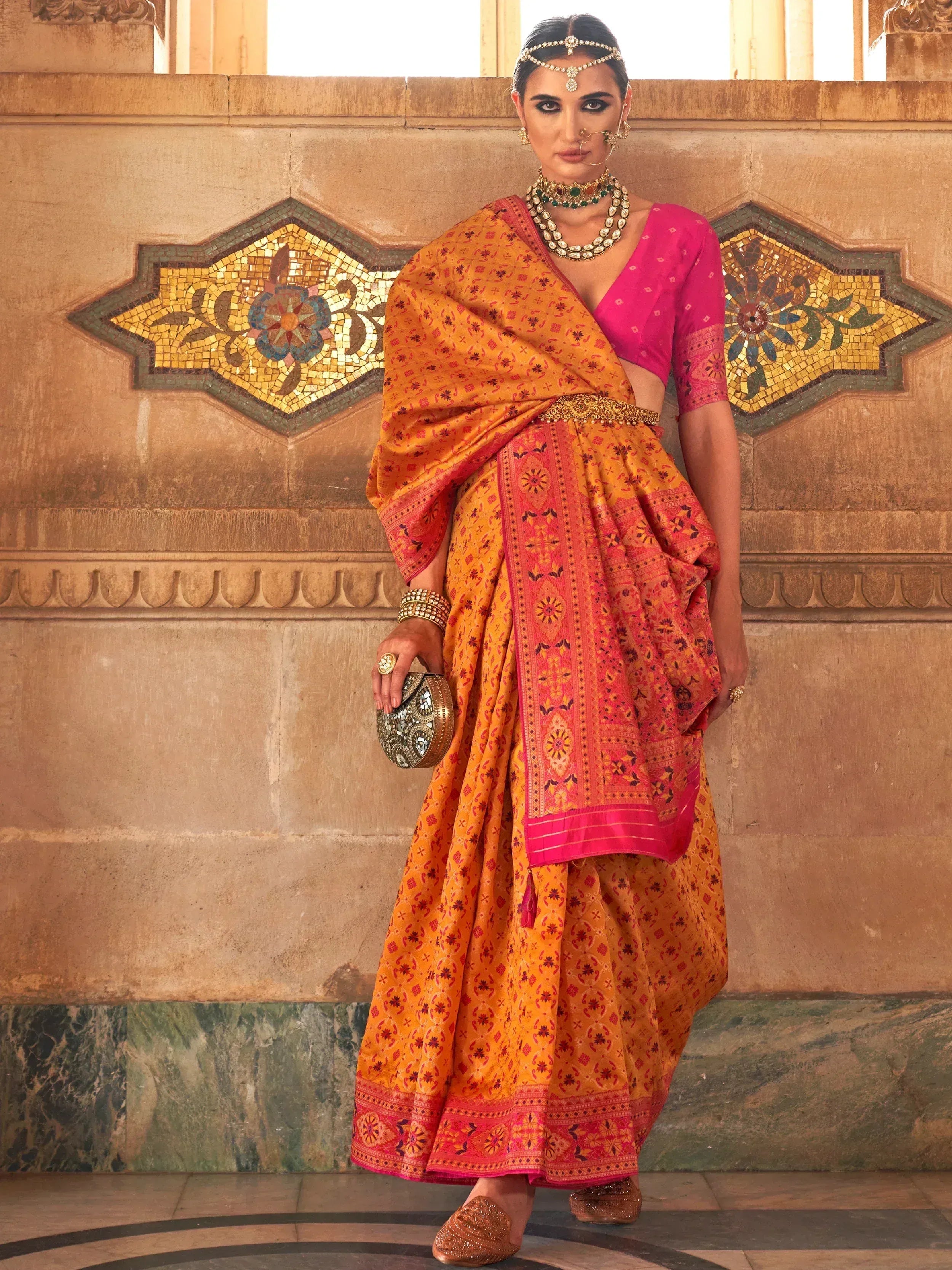 Woman in vibrant orange and pink printed saree with gold jewelry, styled for Indian ethnic wear