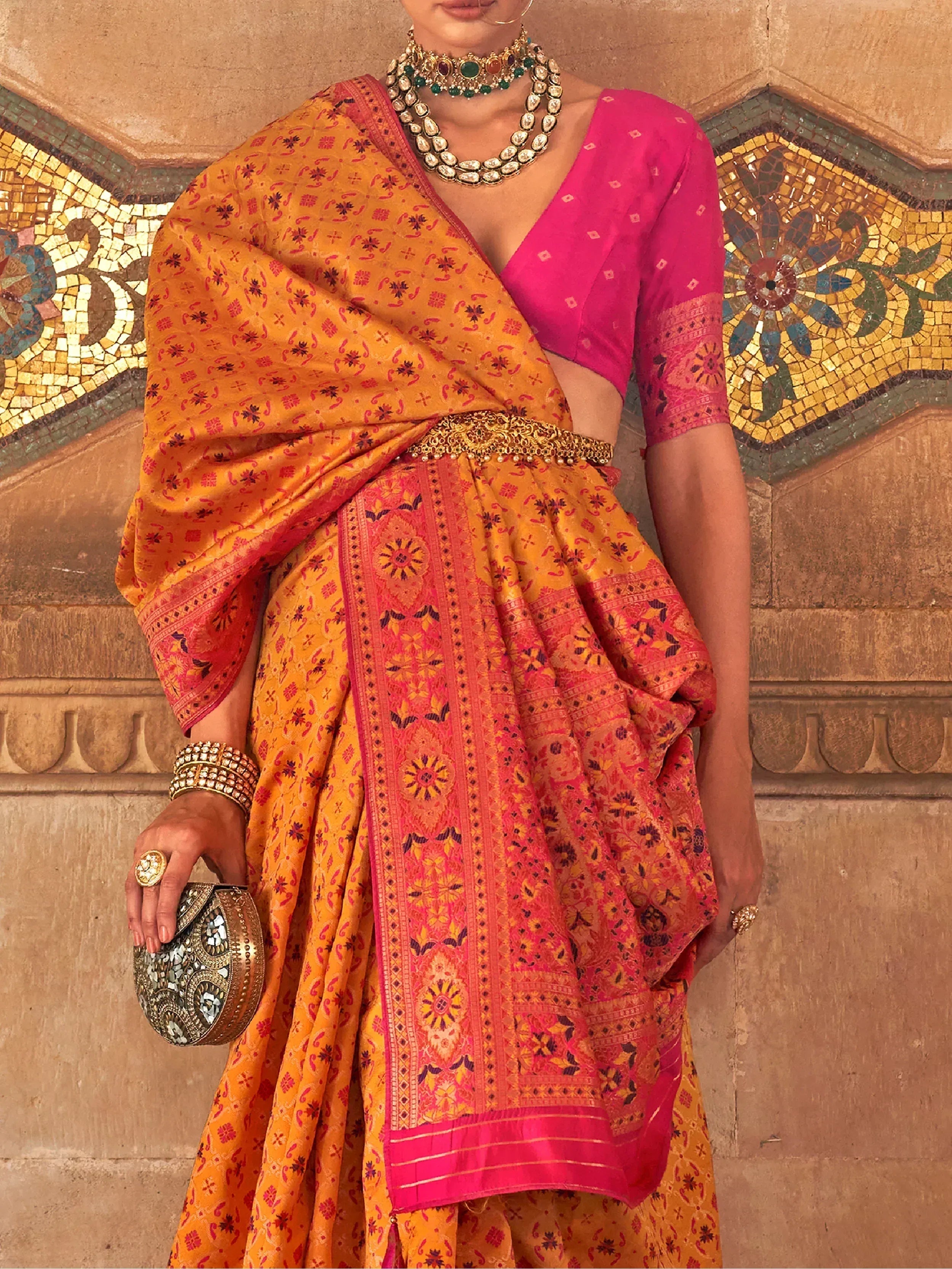 Woman in vibrant orange and pink printed lehenga choli with gold jewelry, styled for Indian ethnic wear