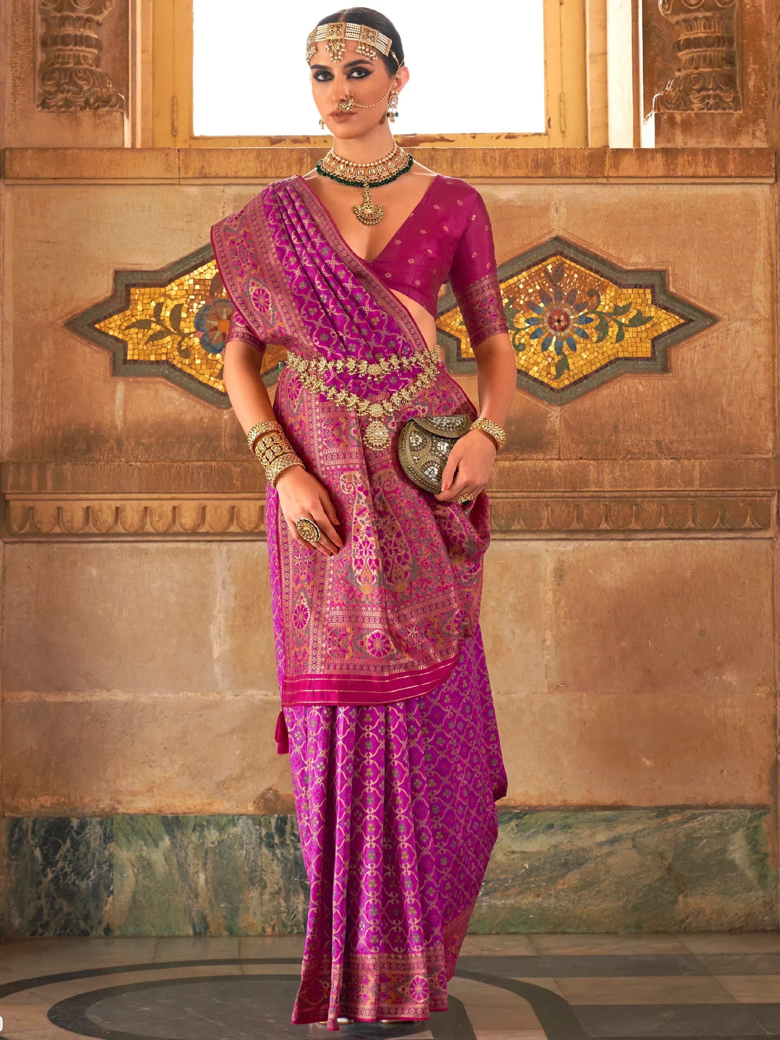 Woman in vibrant pink designer saree with gold embroidery, traditional jewelry, and ethnic accessories