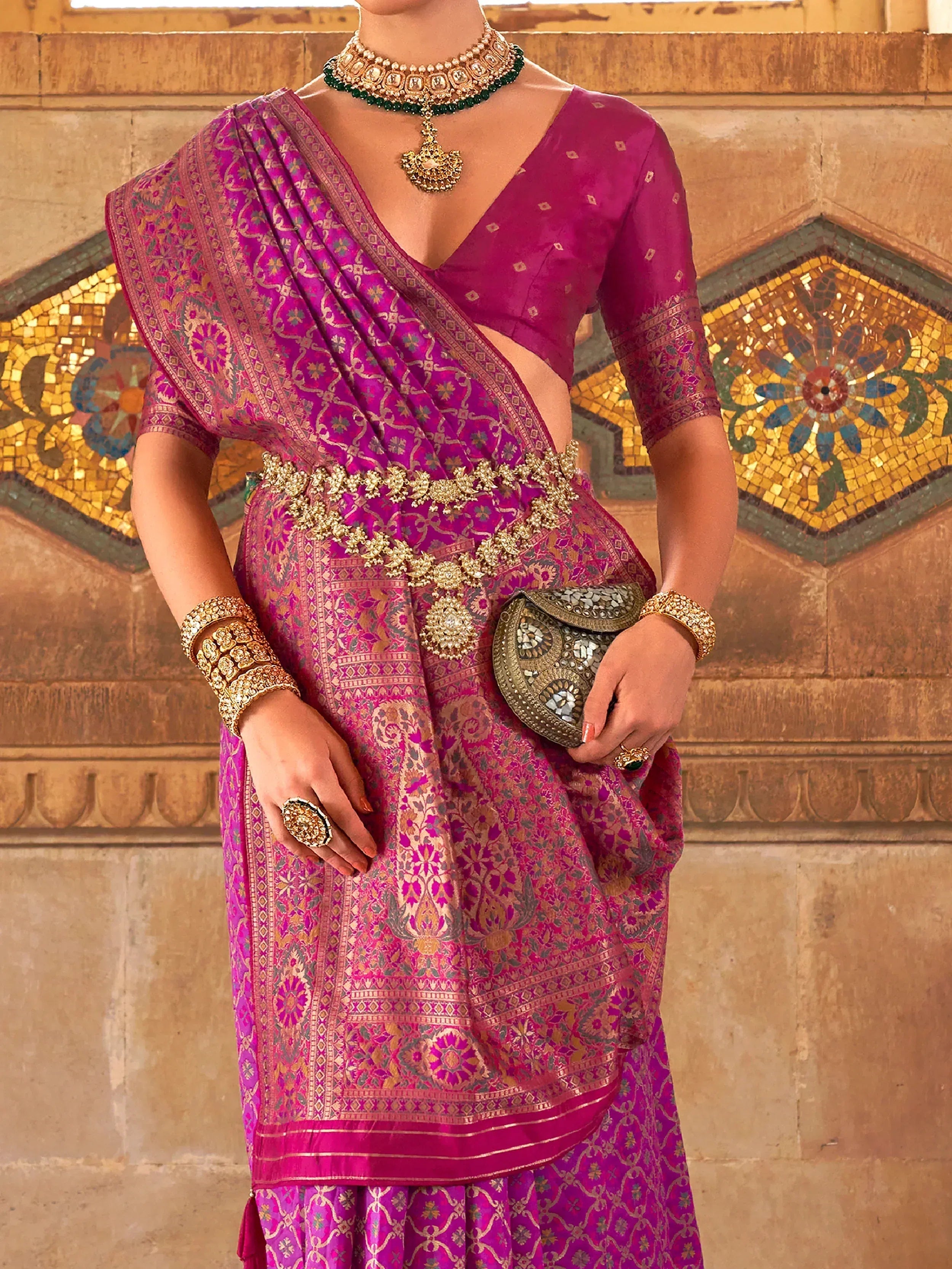 Elegant purple designer saree with gold embroidery, paired with traditional jewelry and a mirror-work clutch.