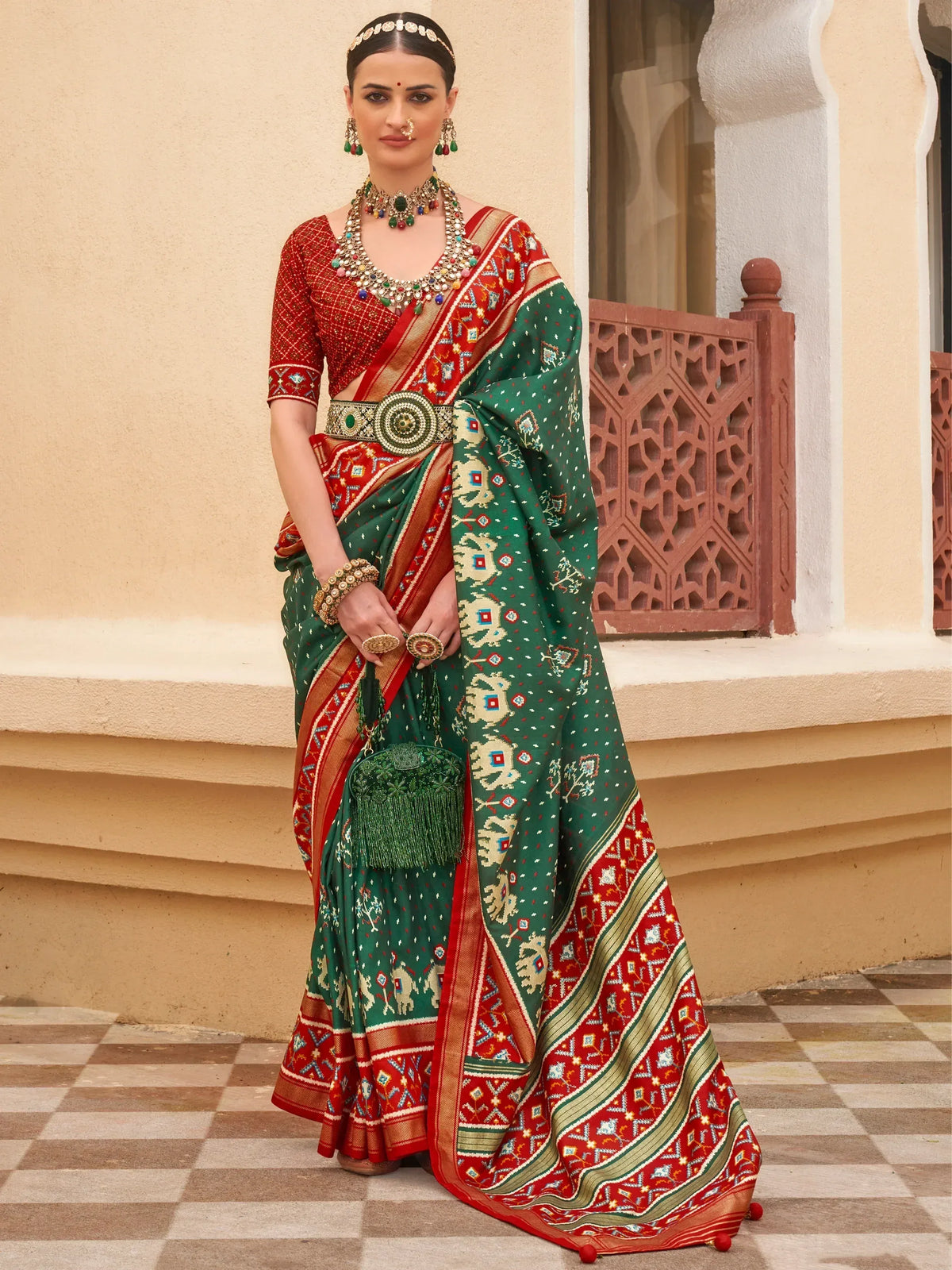 Woman in traditional Indian saree with red and green geometric patterns, ethnic jewelry, and matching clutch