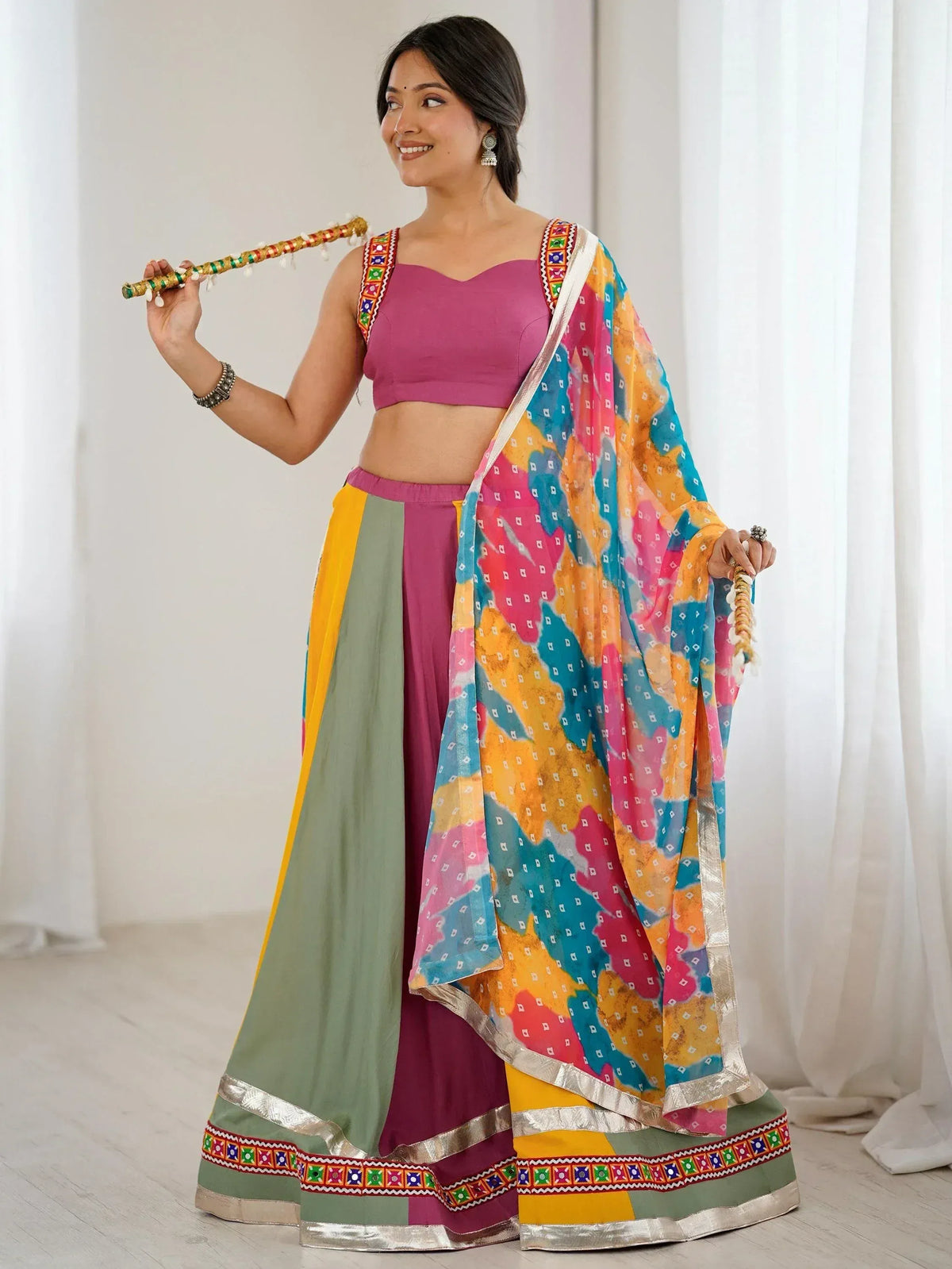 Woman in colorful Indian ethnic wear with embroidered lehenga choli and dupatta, holding decorative stick