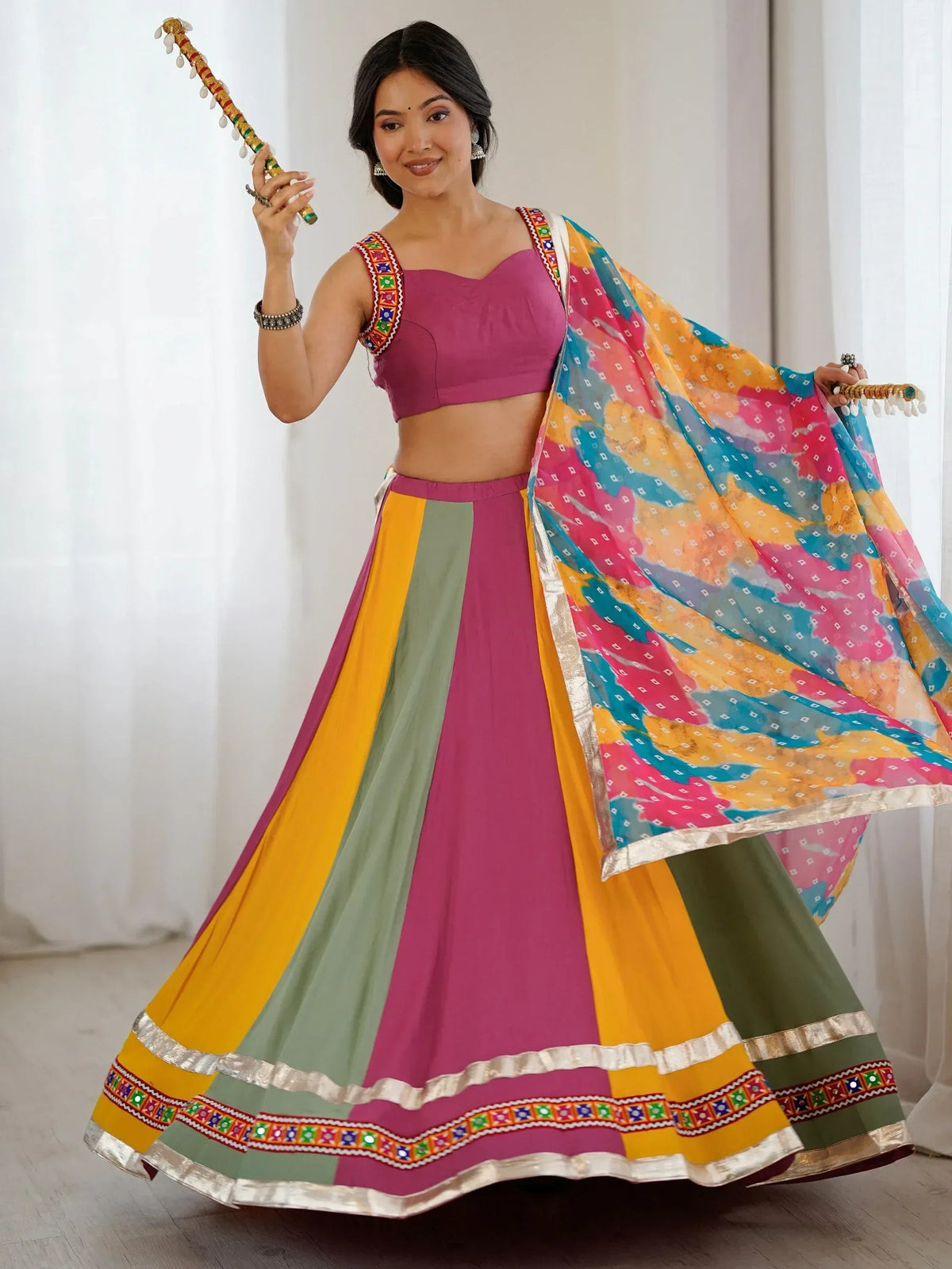 Woman in vibrant Indian lehenga choli with colorful dupatta and traditional dandiya sticks, perfect for festive occasions.