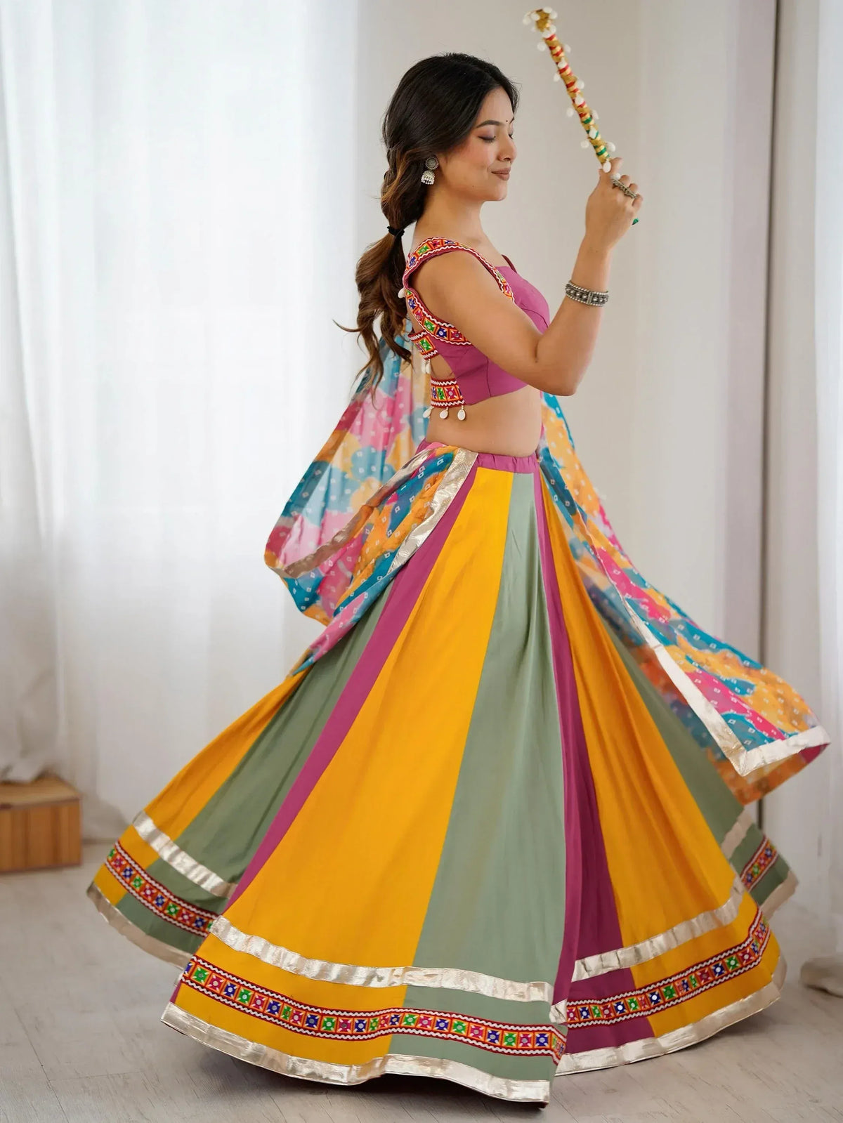 Woman in colorful Indian lehenga choli with mirror work, dancing with dandiya stick