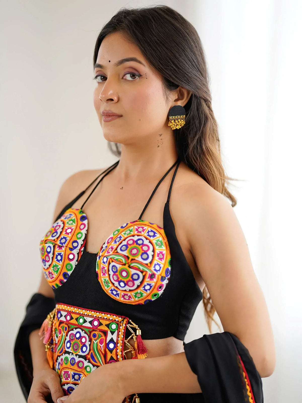 Woman in black halter top with colorful mirror embroidery, ethnic Indian wear, matching earrings