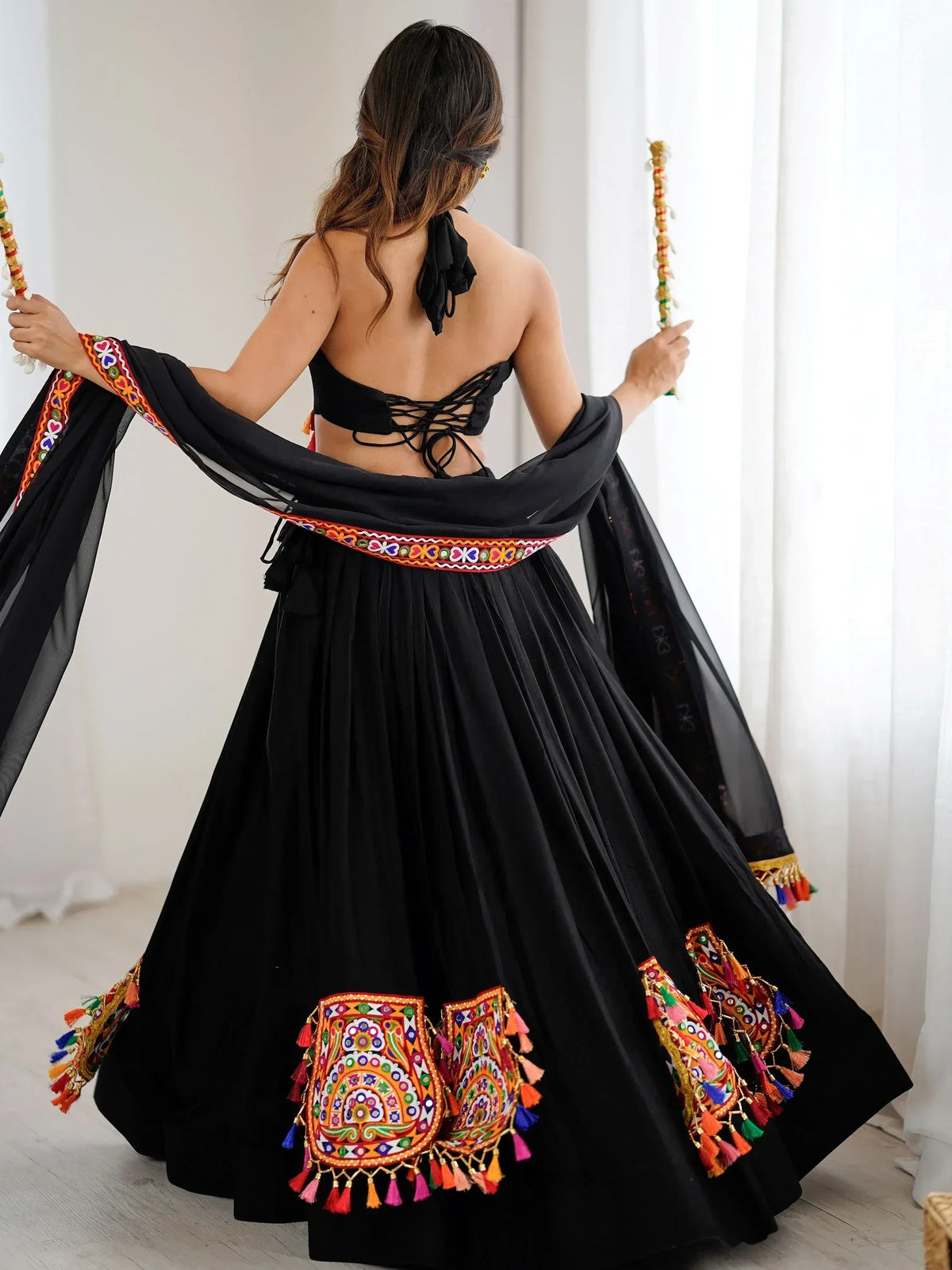 Black ethnic lehenga choli with colorful mirror work, tassels, and back lace-up design, perfect for festive occasions.