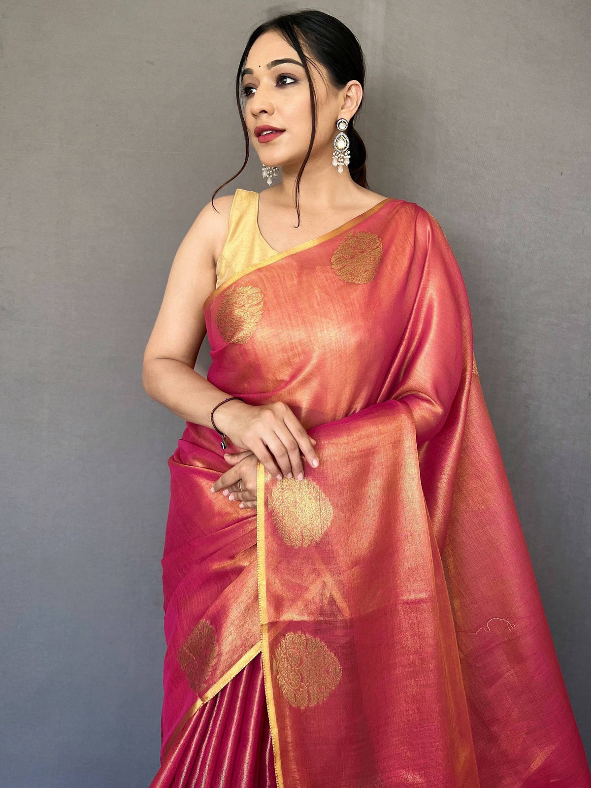 Woman in vibrant pink and gold Indian saree with floral motifs, styled with traditional earrings