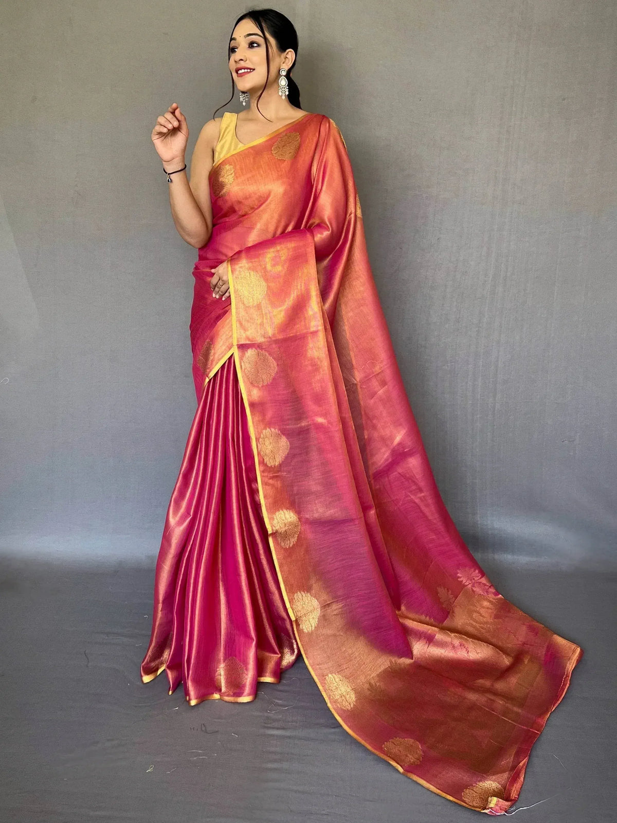 Woman in vibrant pink and orange silk saree with gold floral motifs, perfect for Indian ethnic wear occasions.