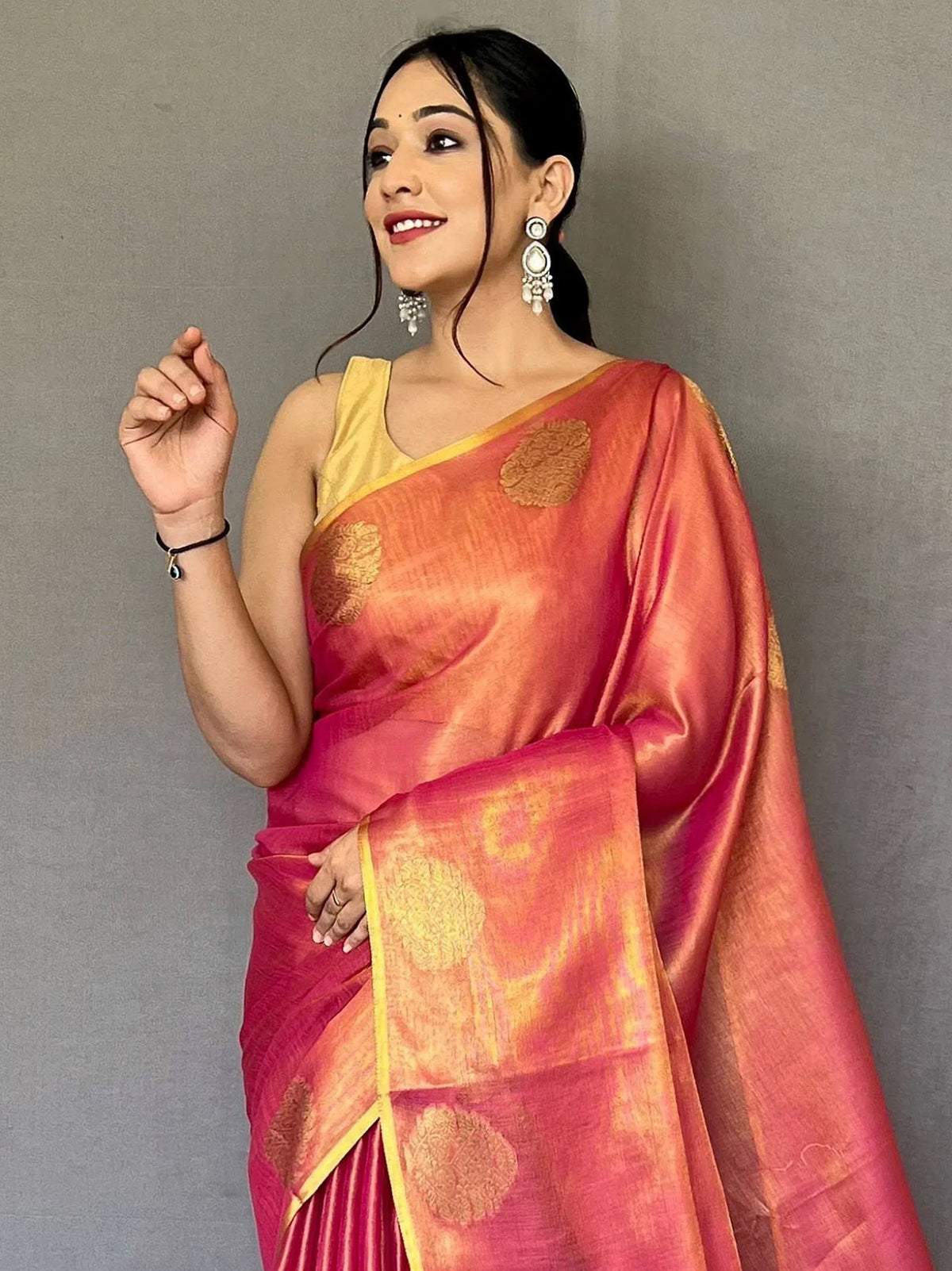 Woman in vibrant pink and orange designer saree with gold motifs, paired with yellow blouse and statement earrings