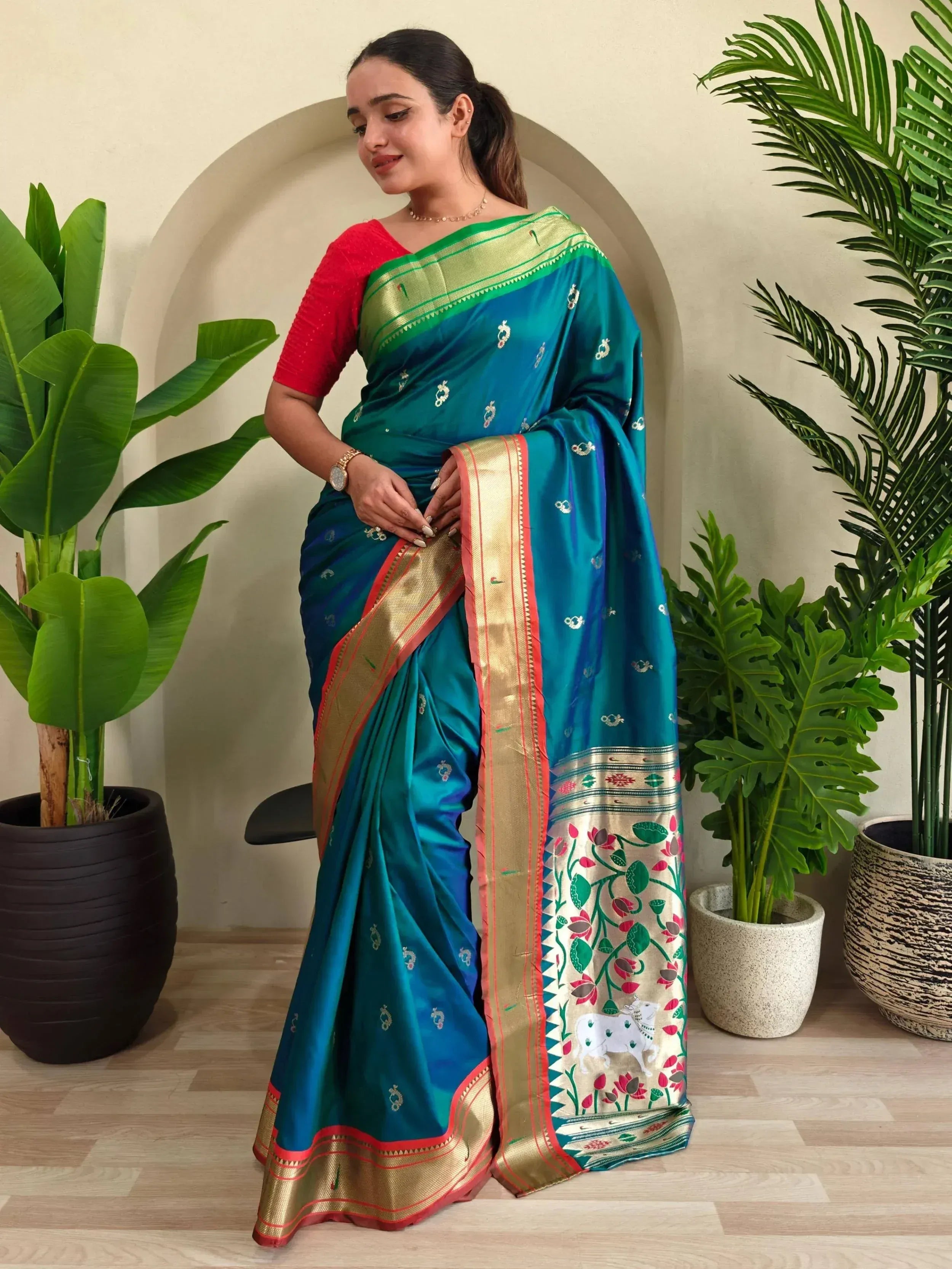 Teal silk saree with gold border and floral motifs, paired with red blouse, ideal for Indian ethnic occasions.