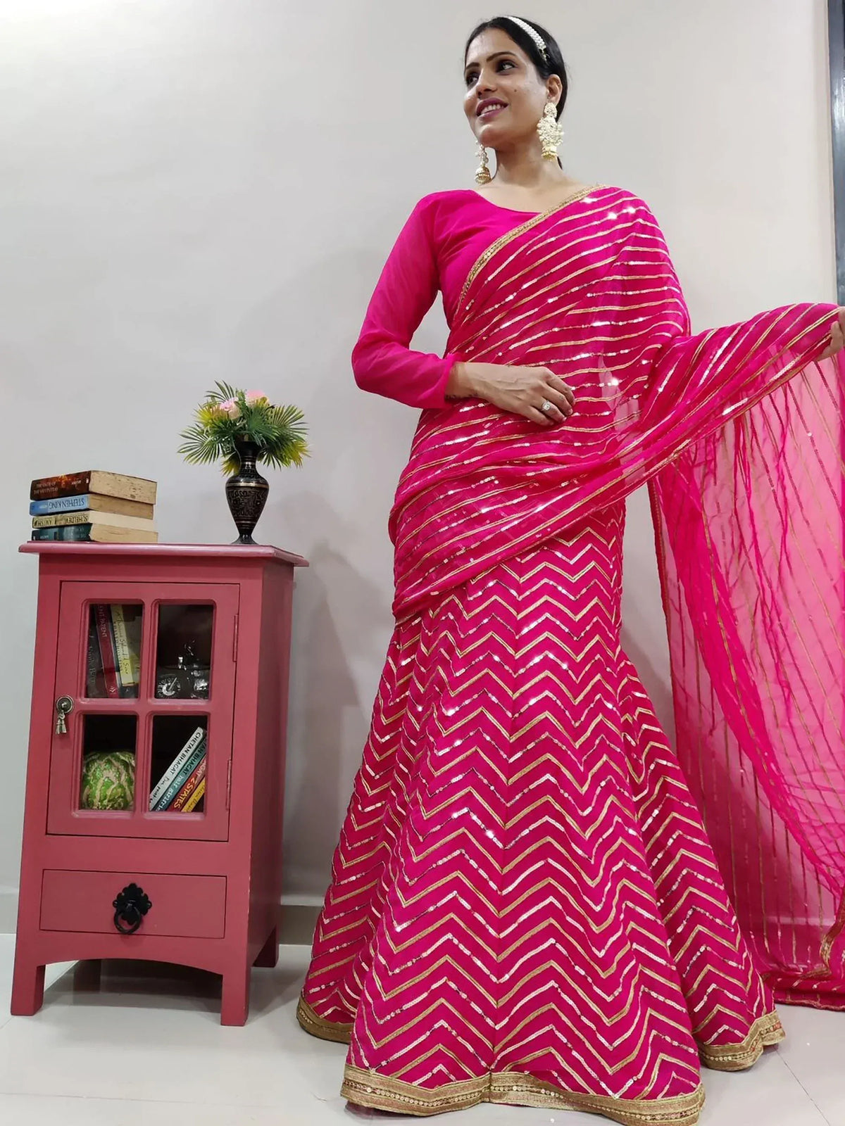 Pink sequin chevron saree with gold trim, styled with matching blouse and statement earrings for festive occasions.
