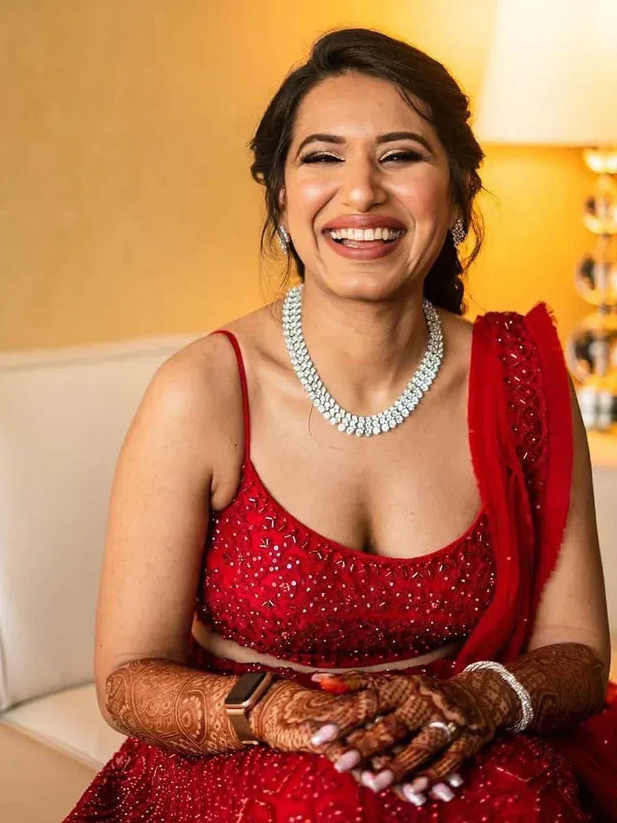 Smiling woman in red embroidered lehenga choli with henna hands and diamond necklace