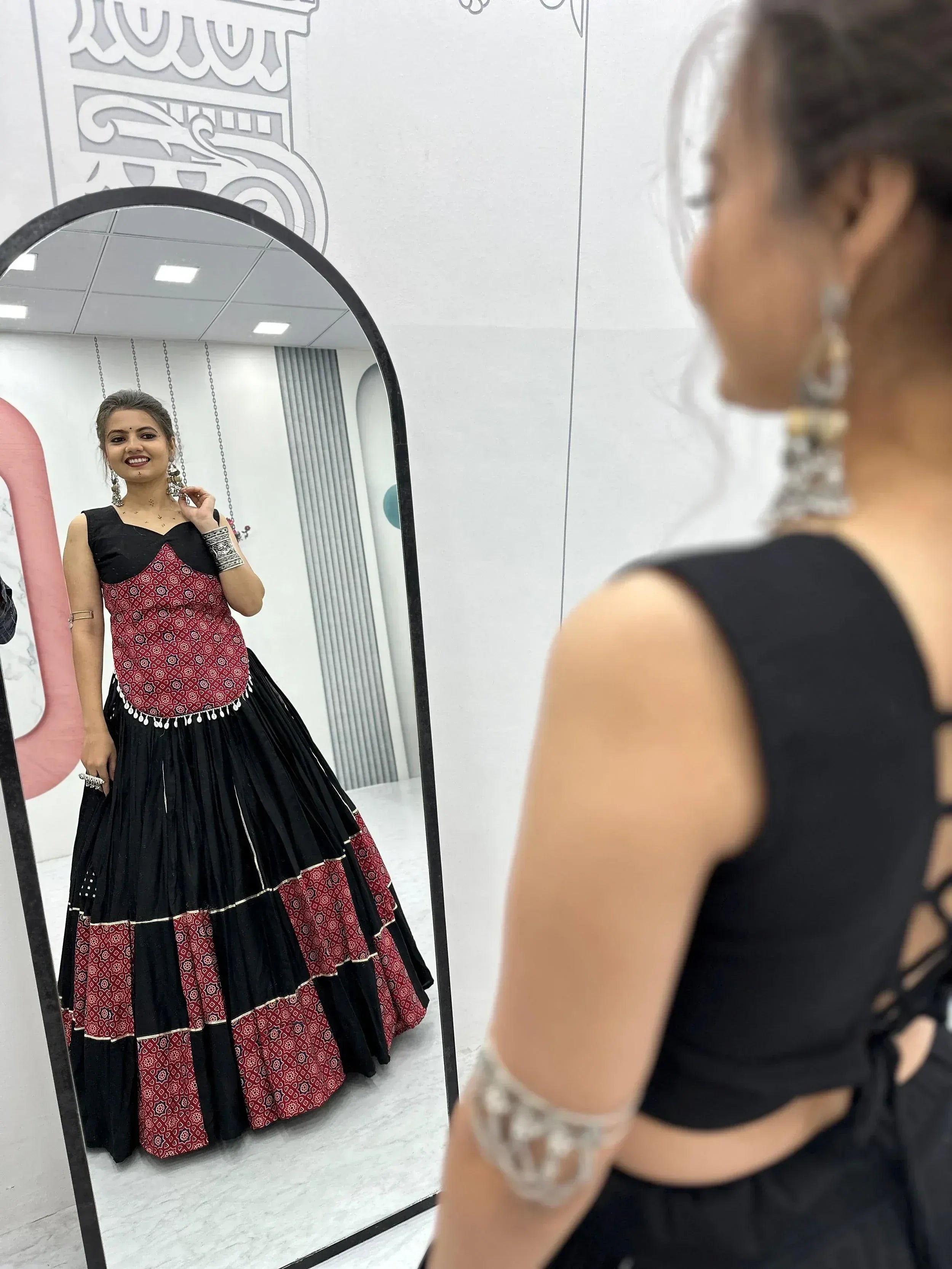 Woman admiring herself in mirror wearing black and red printed ethnic gown with layered skirt