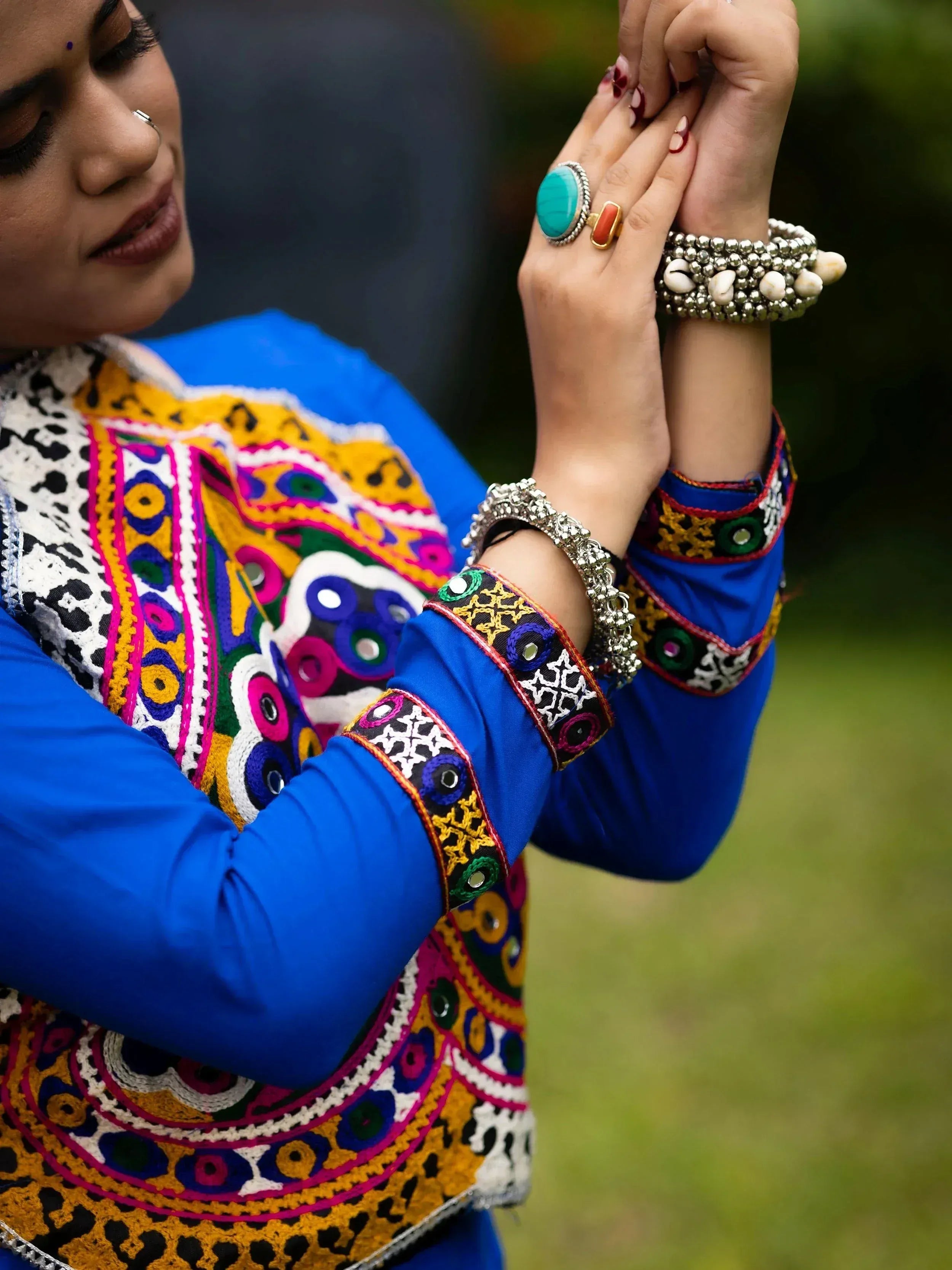 Woman in vibrant blue ethnic wear with mirror embroidery, statement rings, and traditional bangles.