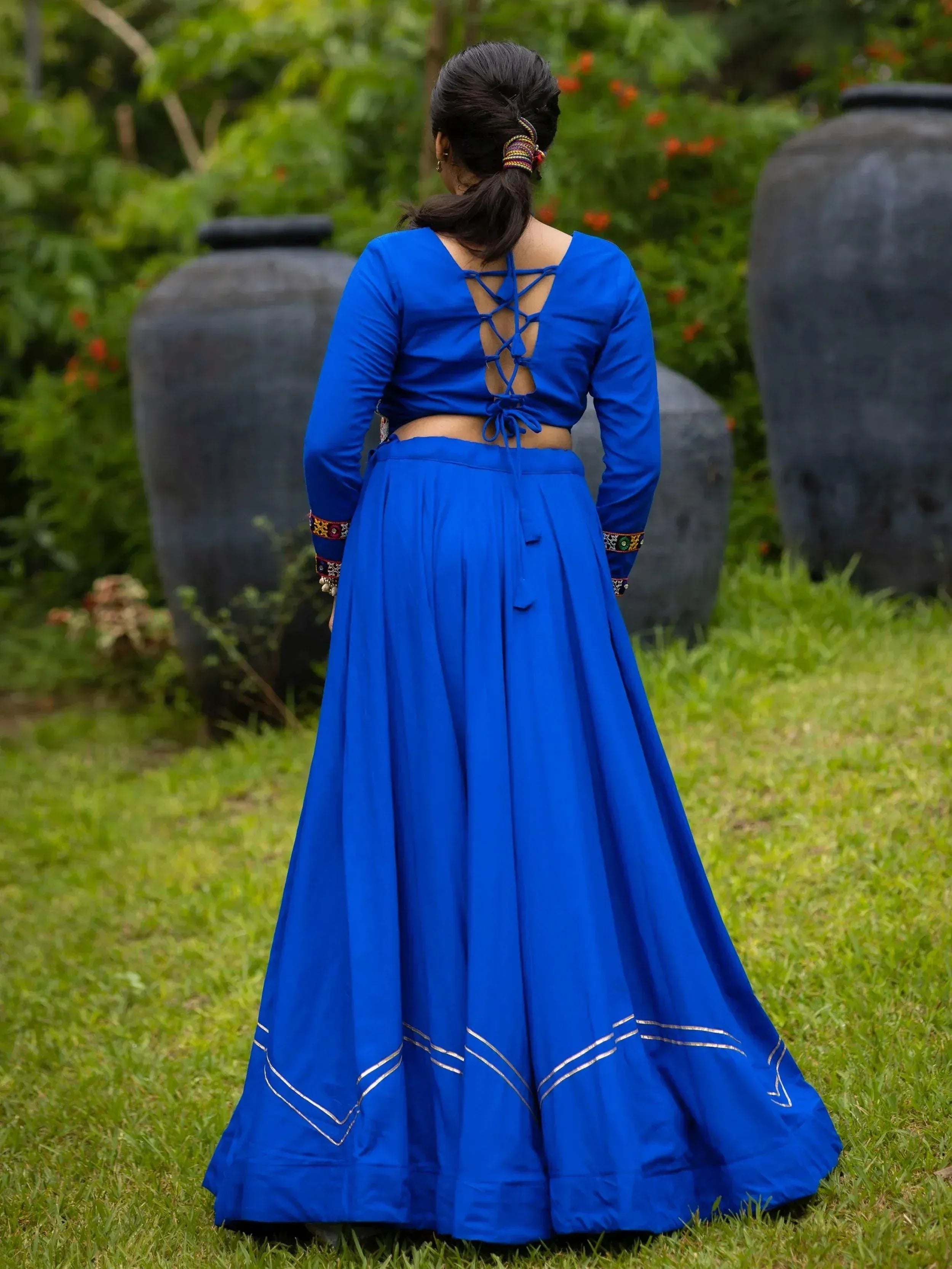 Royal blue ethnic lehenga choli with crisscross back and gold trim, worn outdoors on grass