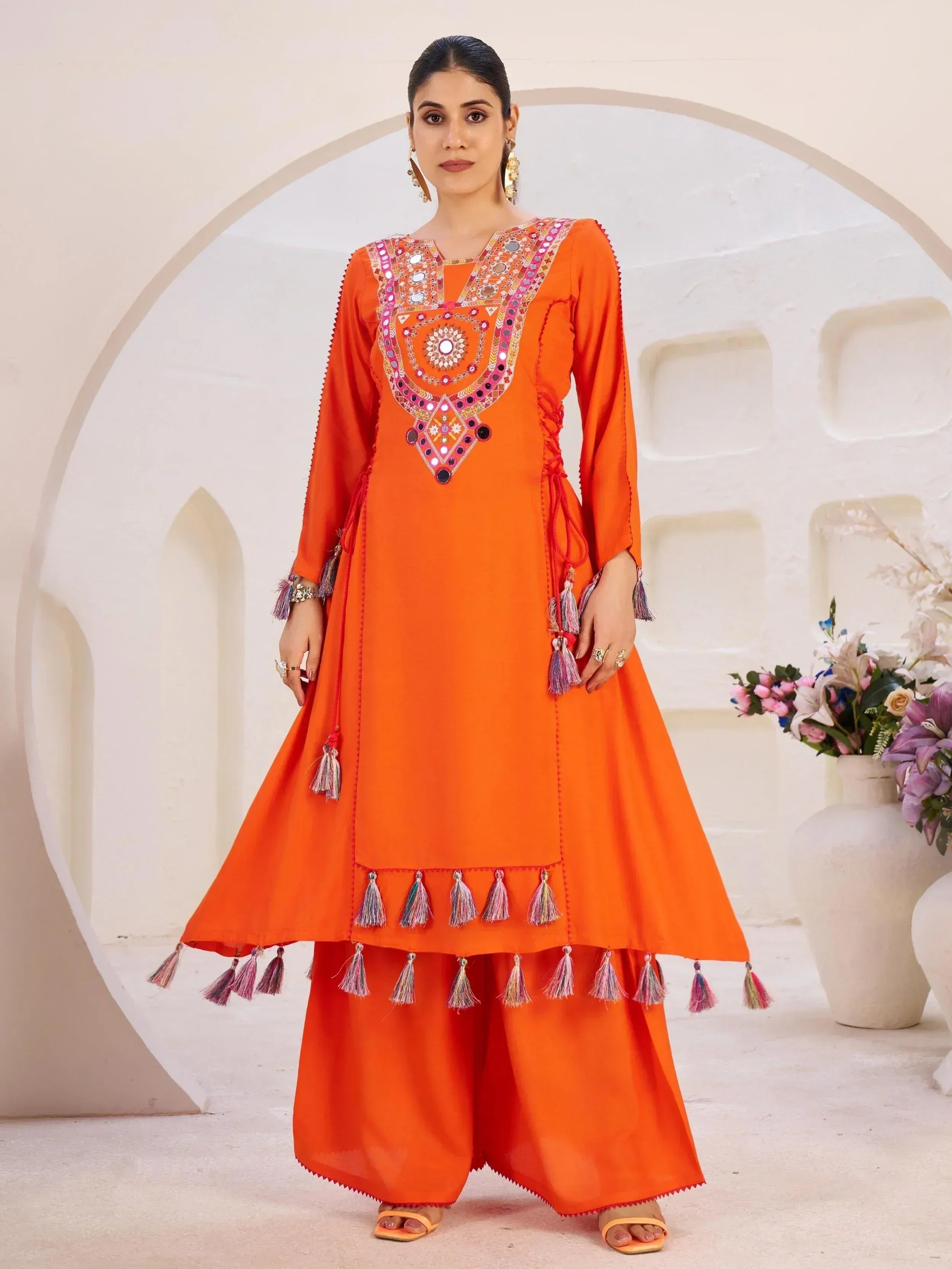 Vibrant orange ethnic salwar kameez with mirror work and tassels, perfect for festive occasions.