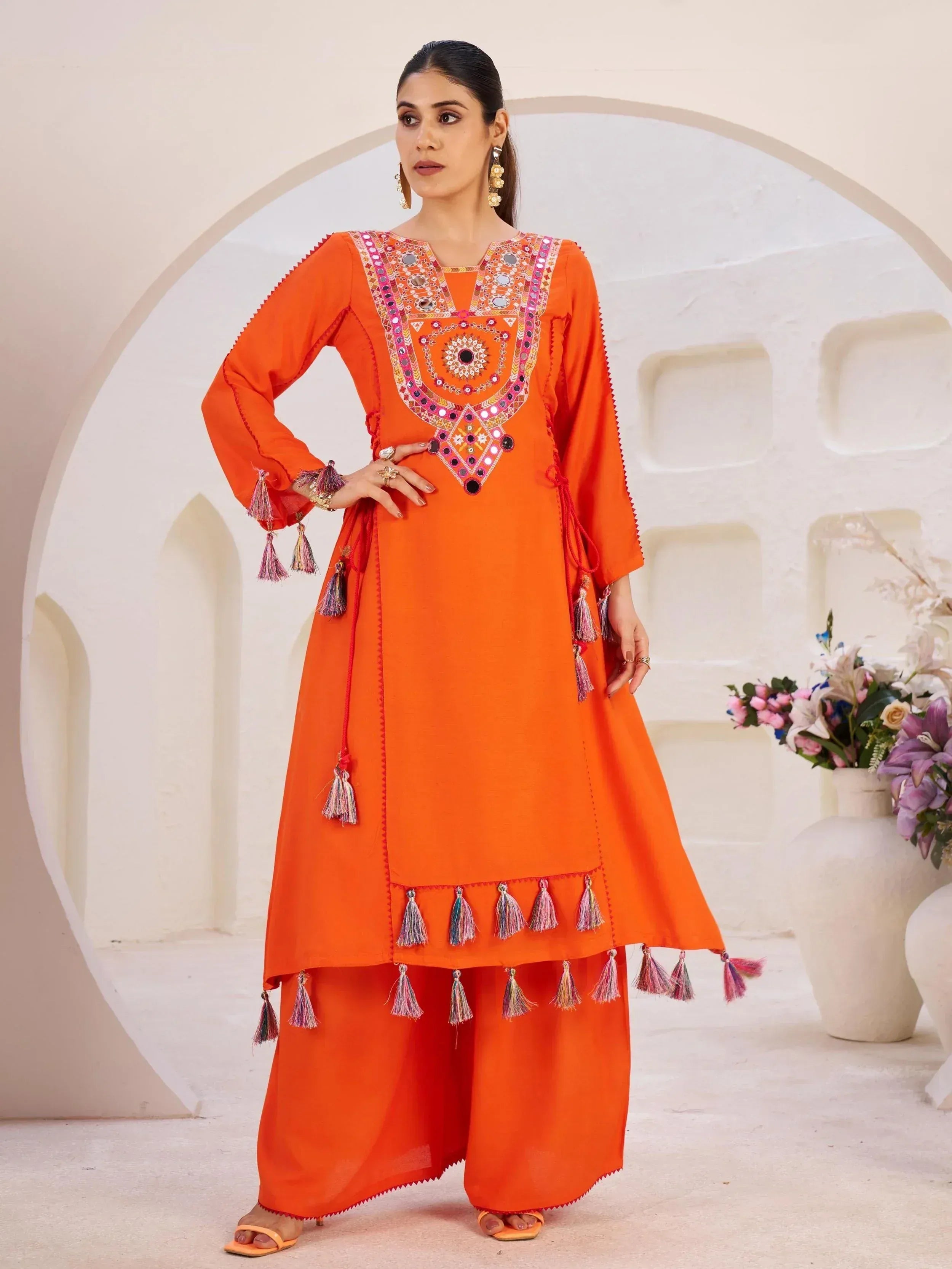 Orange ethnic kurta with mirror work and tassels, paired with palazzo pants for festive occasions