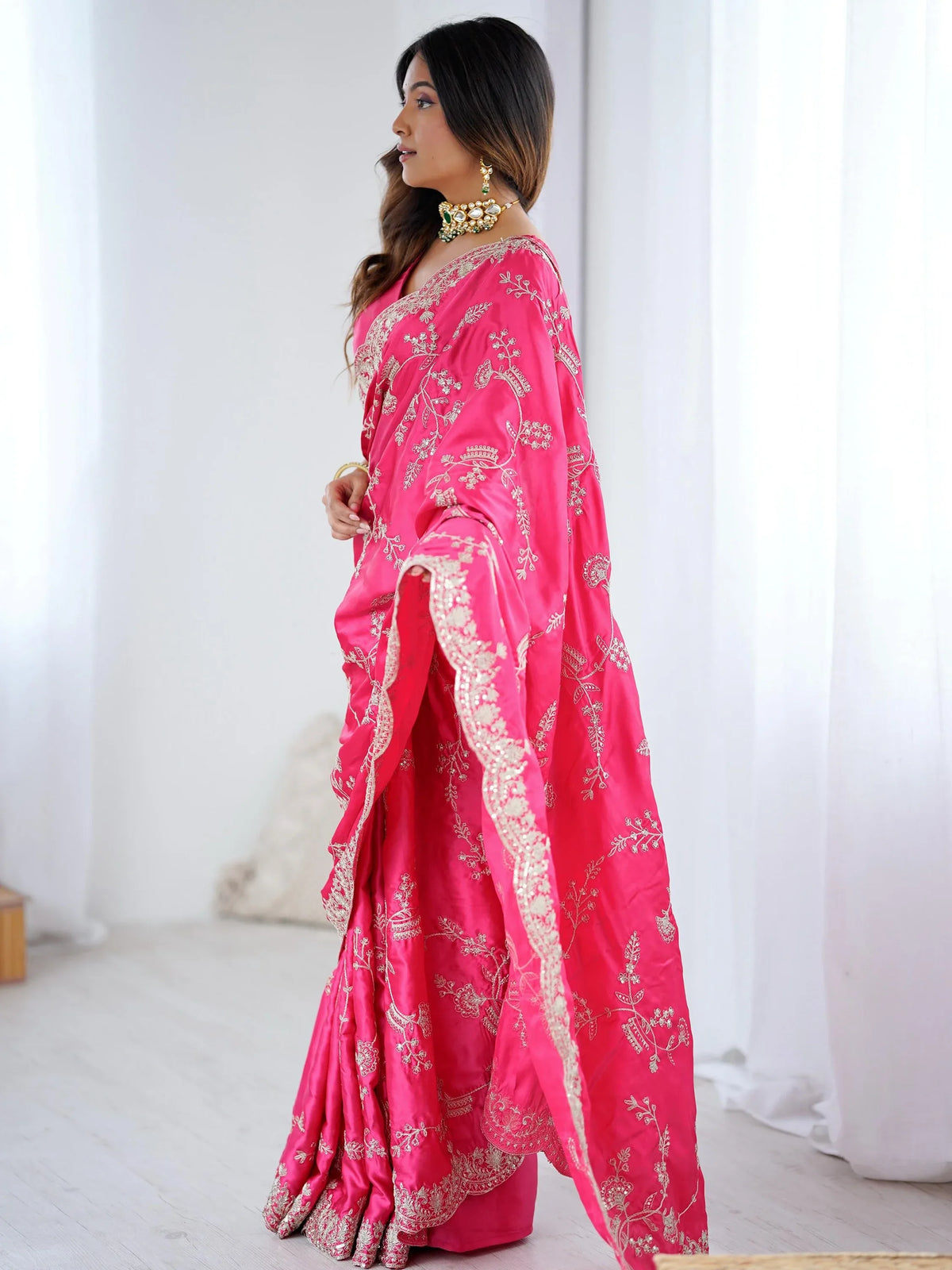 Woman wearing a bright pink designer saree with gold embroidery and traditional jewelry