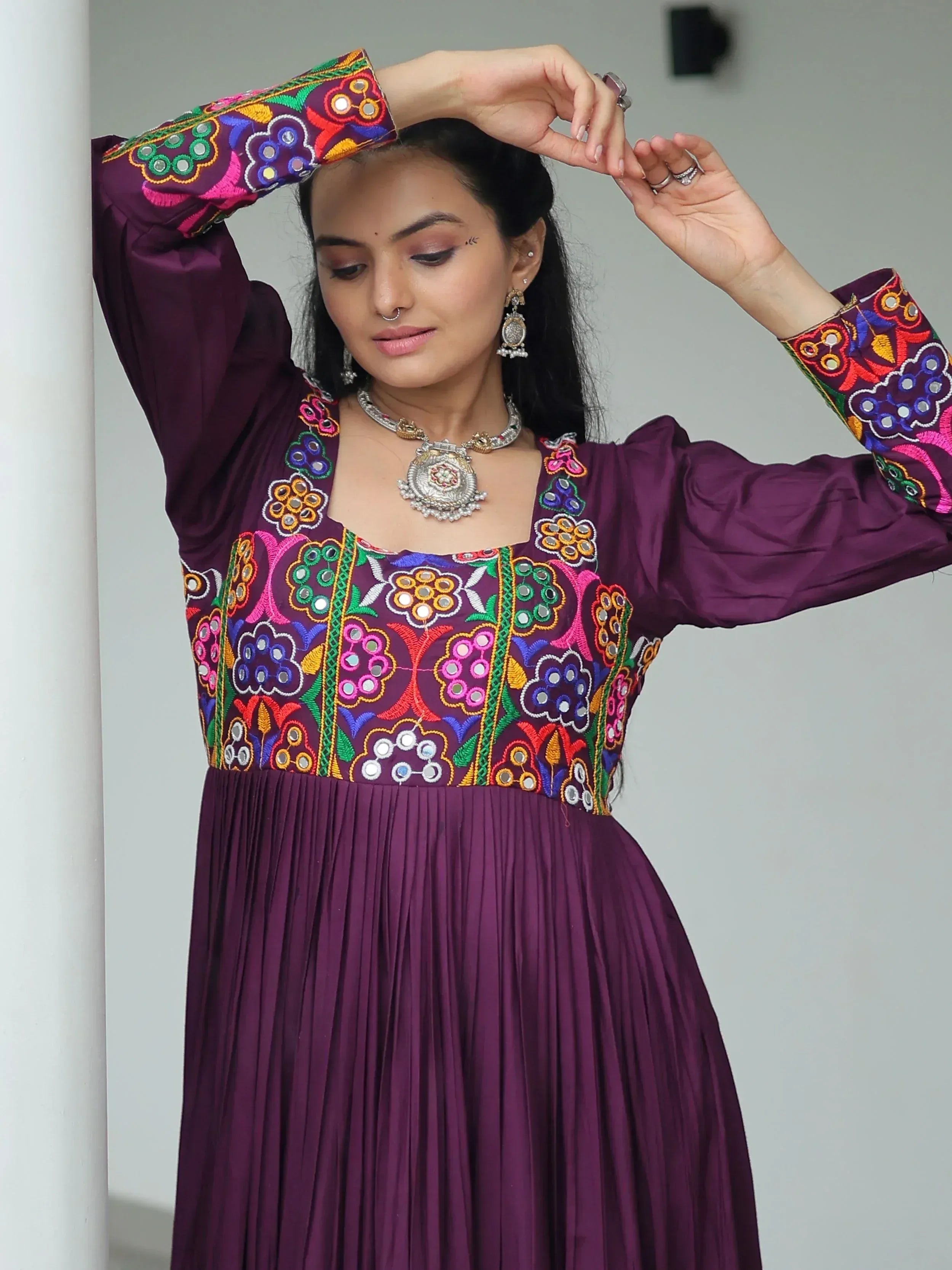 Purple ethnic gown with colorful mirror embroidery and pleated skirt, styled with traditional jewelry